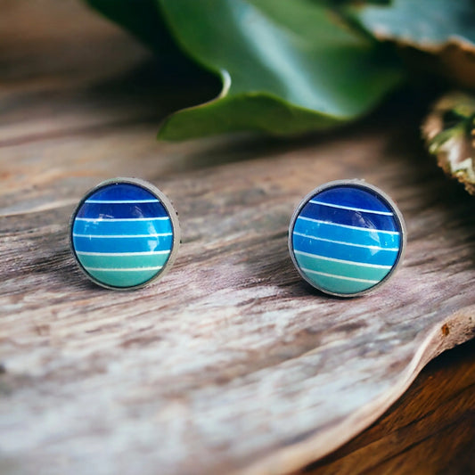 Round blue gradient striped stud earrings in a silver-tone setting displayed on a rustic whitewashed wood surface