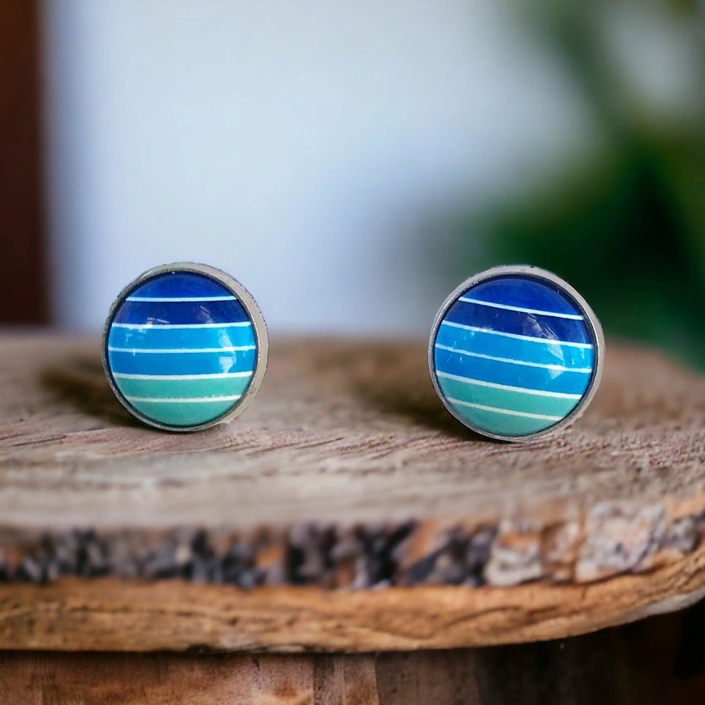 Round blue gradient striped stud earrings in a silver-tone setting displayed on a boho rustic wood surface