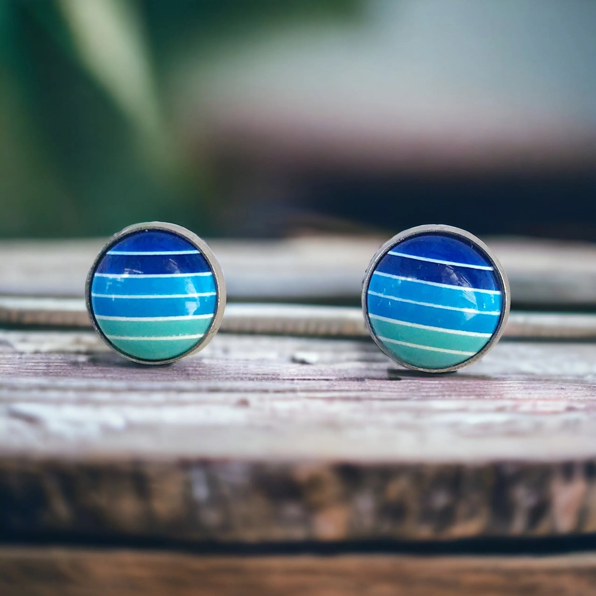 Round blue gradient striped stud earrings in a silver-tone setting displayed on a rustic wood surface