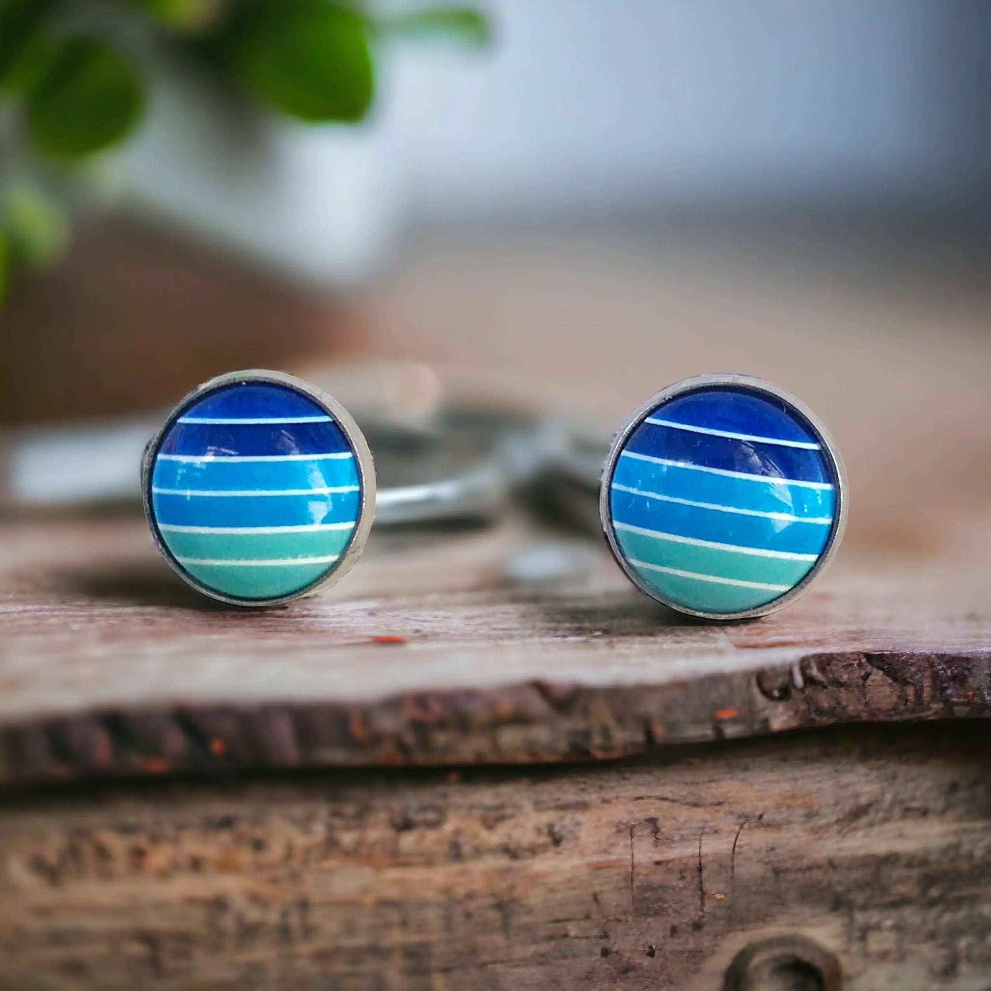 Round blue gradient striped stud earrings in a silver-tone setting displayed on a decorative rustic wood surface