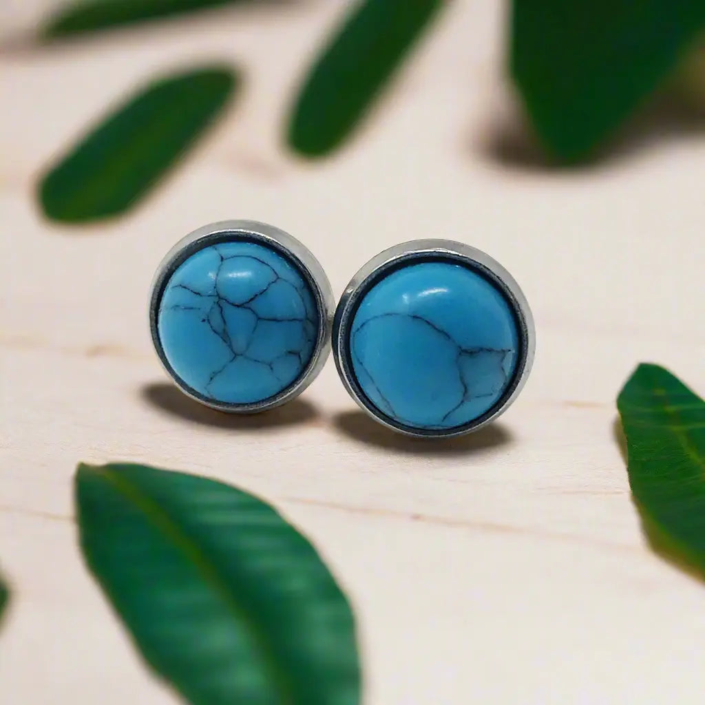 Round blue stone stud earrings in a silver-tone setting on a decorative background