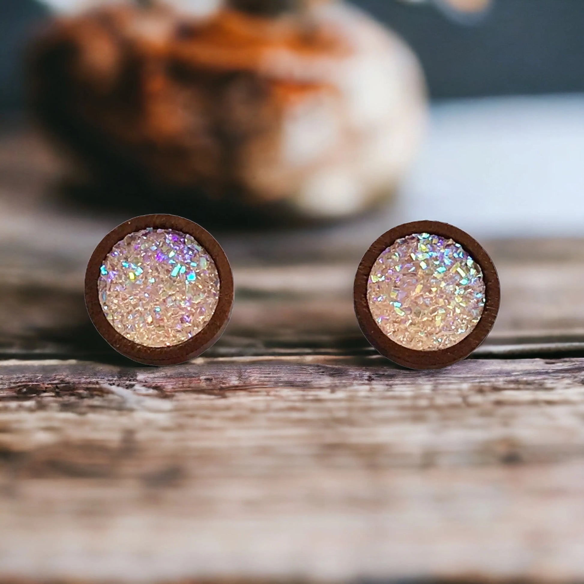 Close-up of round blush pink glitter druzy wood stud earrings displayed on a rustic wood surface