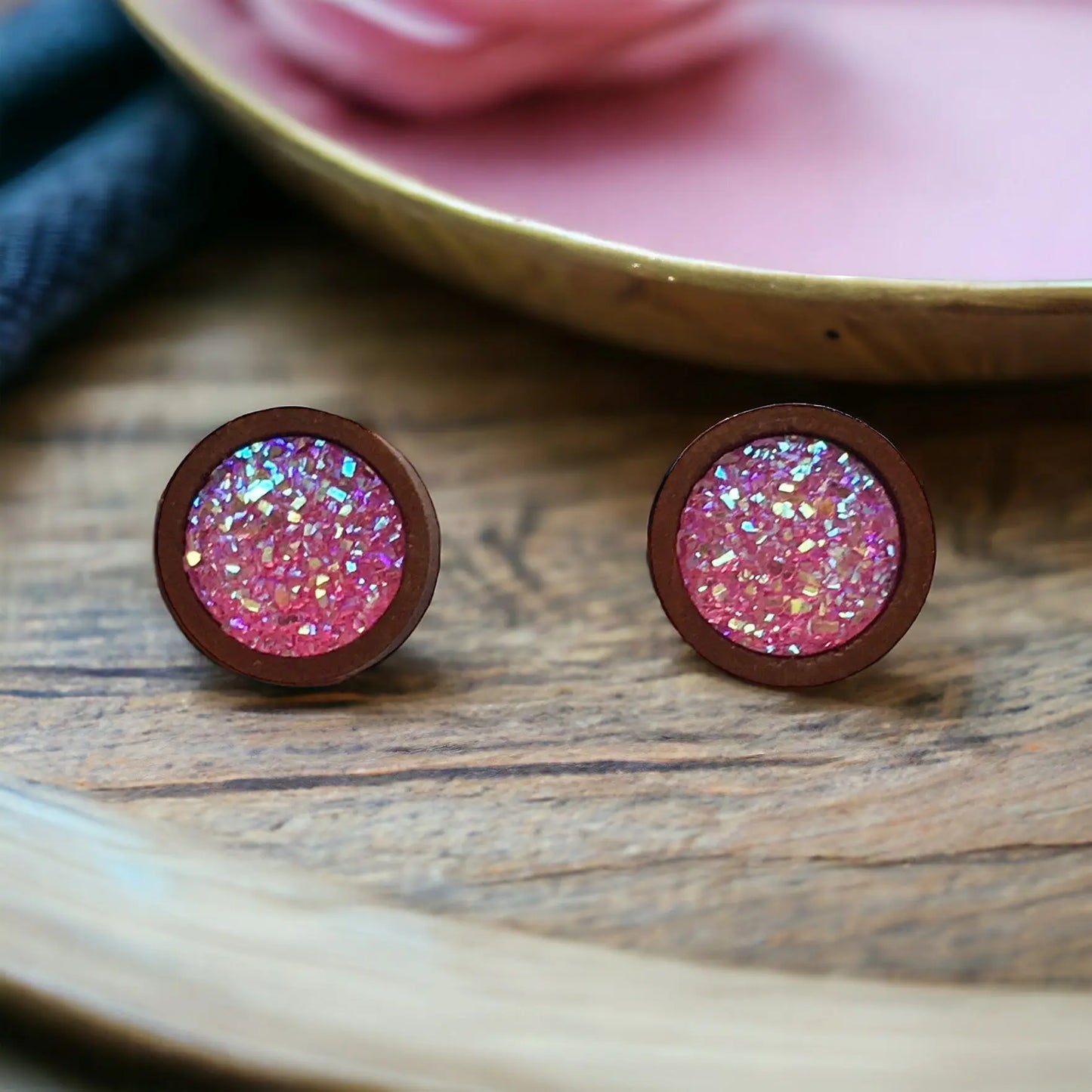 Round bright pink glitter druzy wood stud earrings displayed on a rustic tray