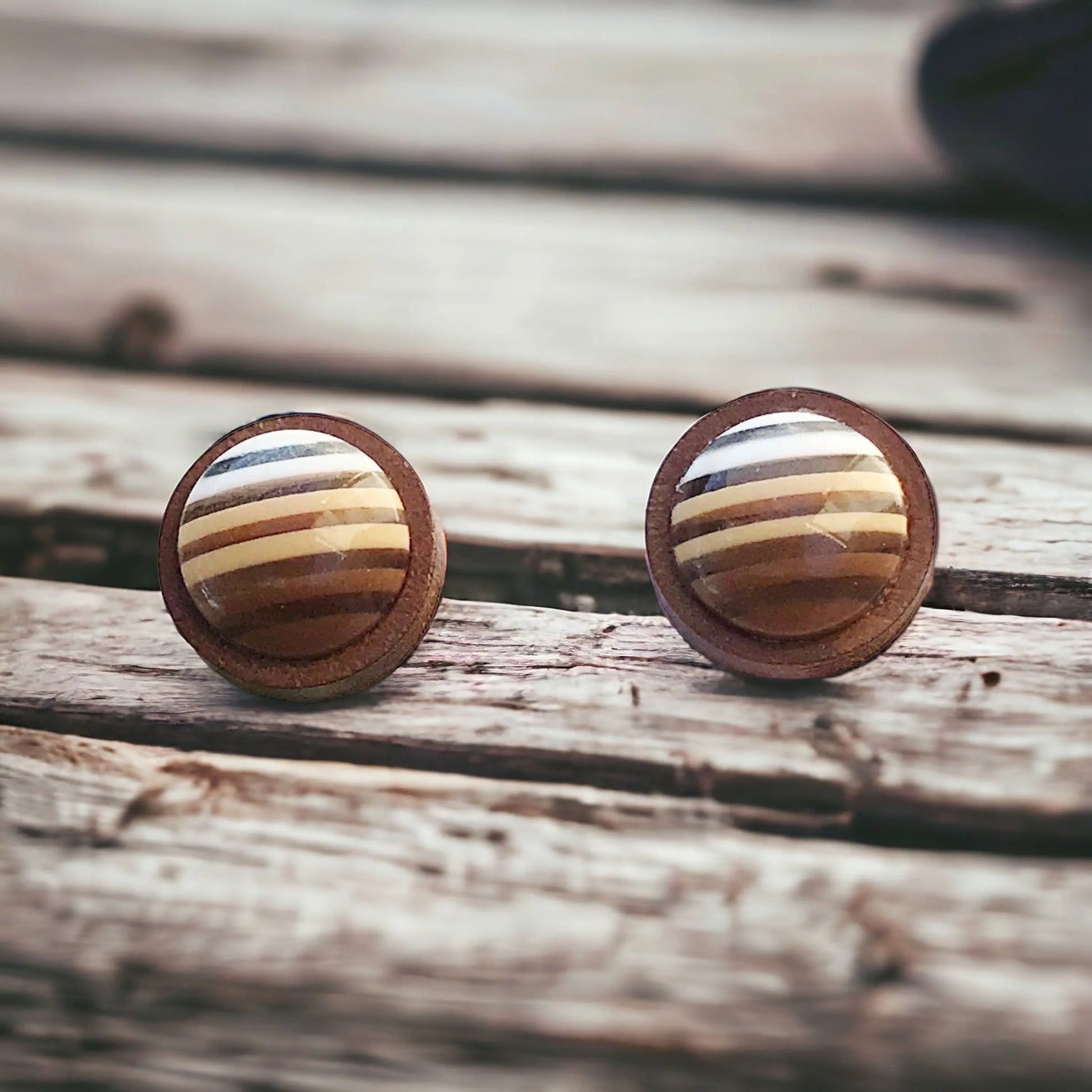 Round brown striped wood stud earrings displayed on a rustic wood surface