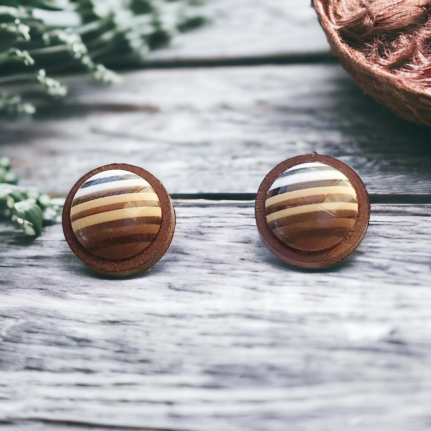 Round brown striped wood stud earrings displayed on a light wood surface