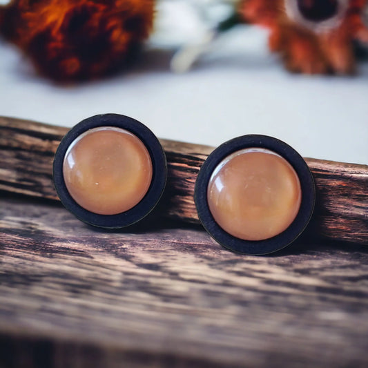 Pair of round earrings with a beige center and black rim on a wooden surface.