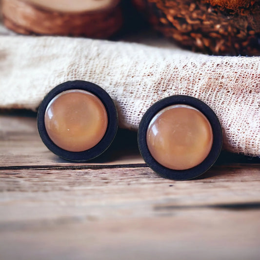Pair of round earrings with brown center and black rim on a textured fabric background
