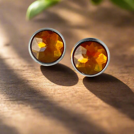 Pair of amber-colored stud earrings on a wooden surface with natural light.