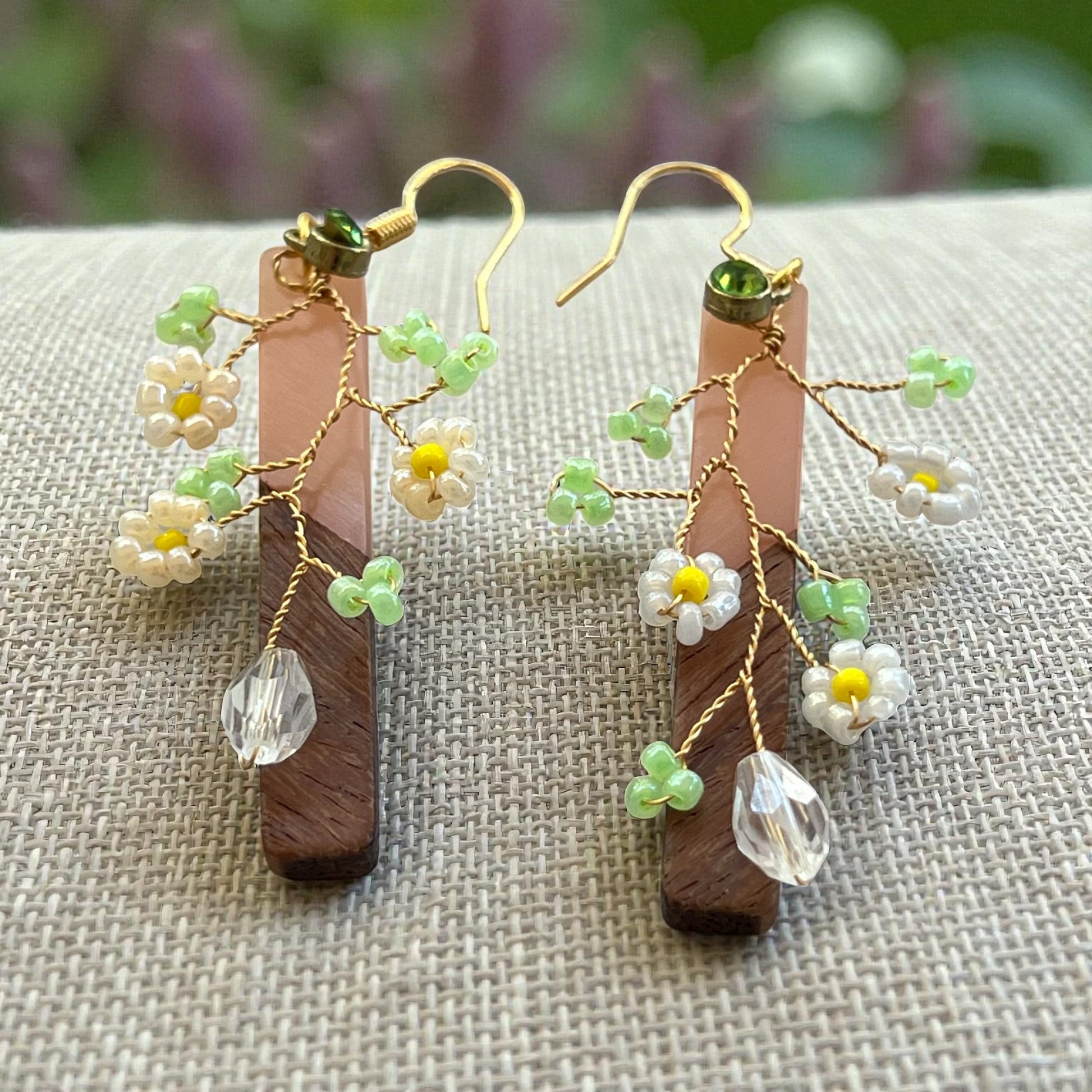 Pair of wooden earrings with floral and crystal details on a textured surface.