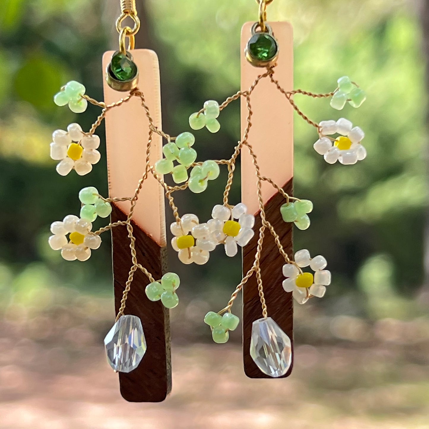 Floral earrings with wooden and crystal elements against a blurred natural background