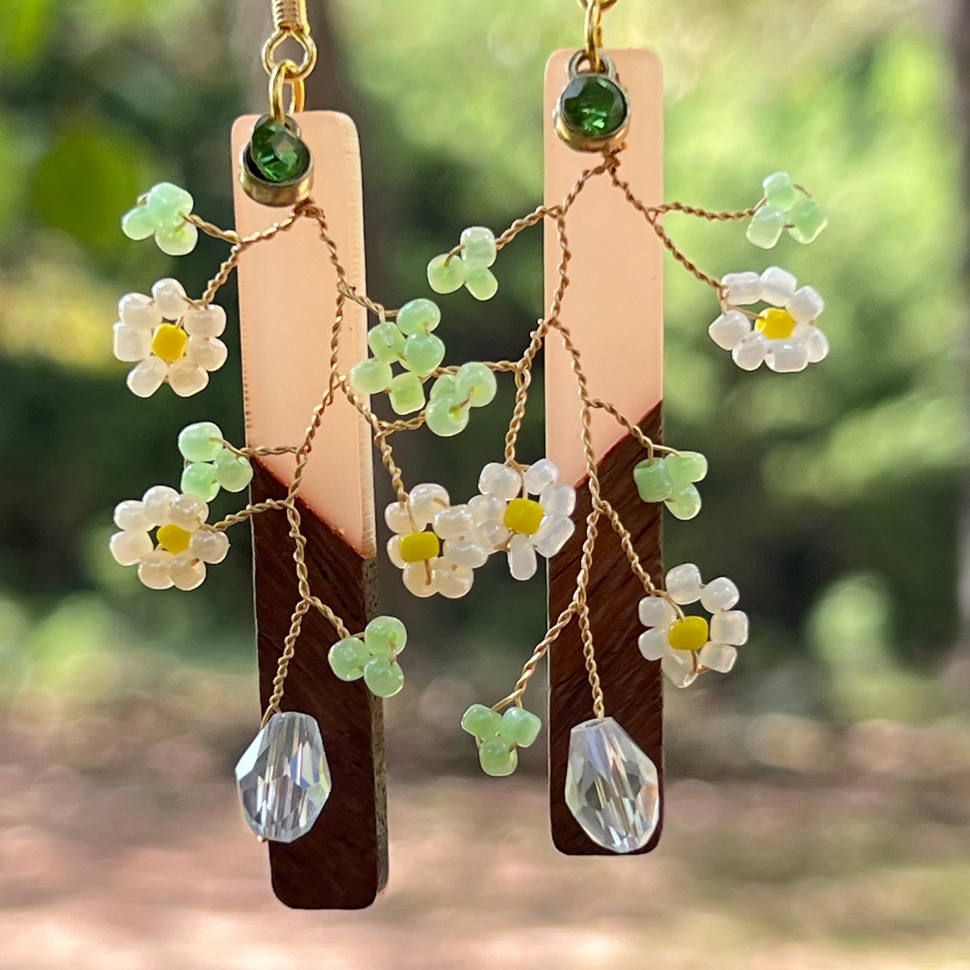 Floral earrings with wooden and crystal elements against a blurred natural background