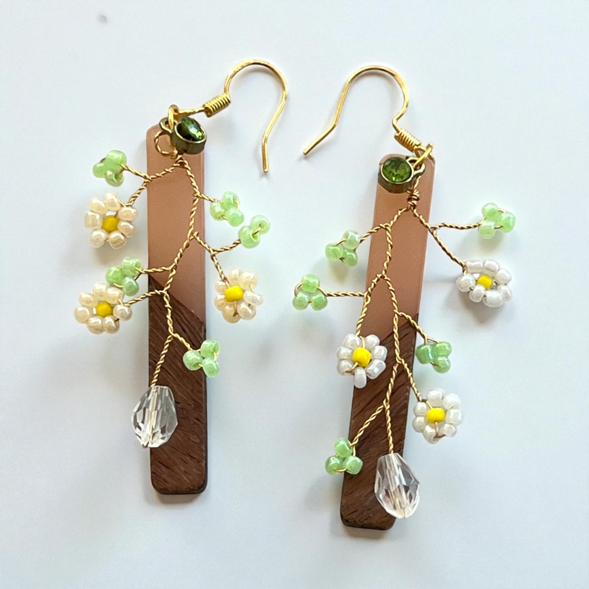 Pair of floral earrings with wooden sticks and crystal beads on a white background