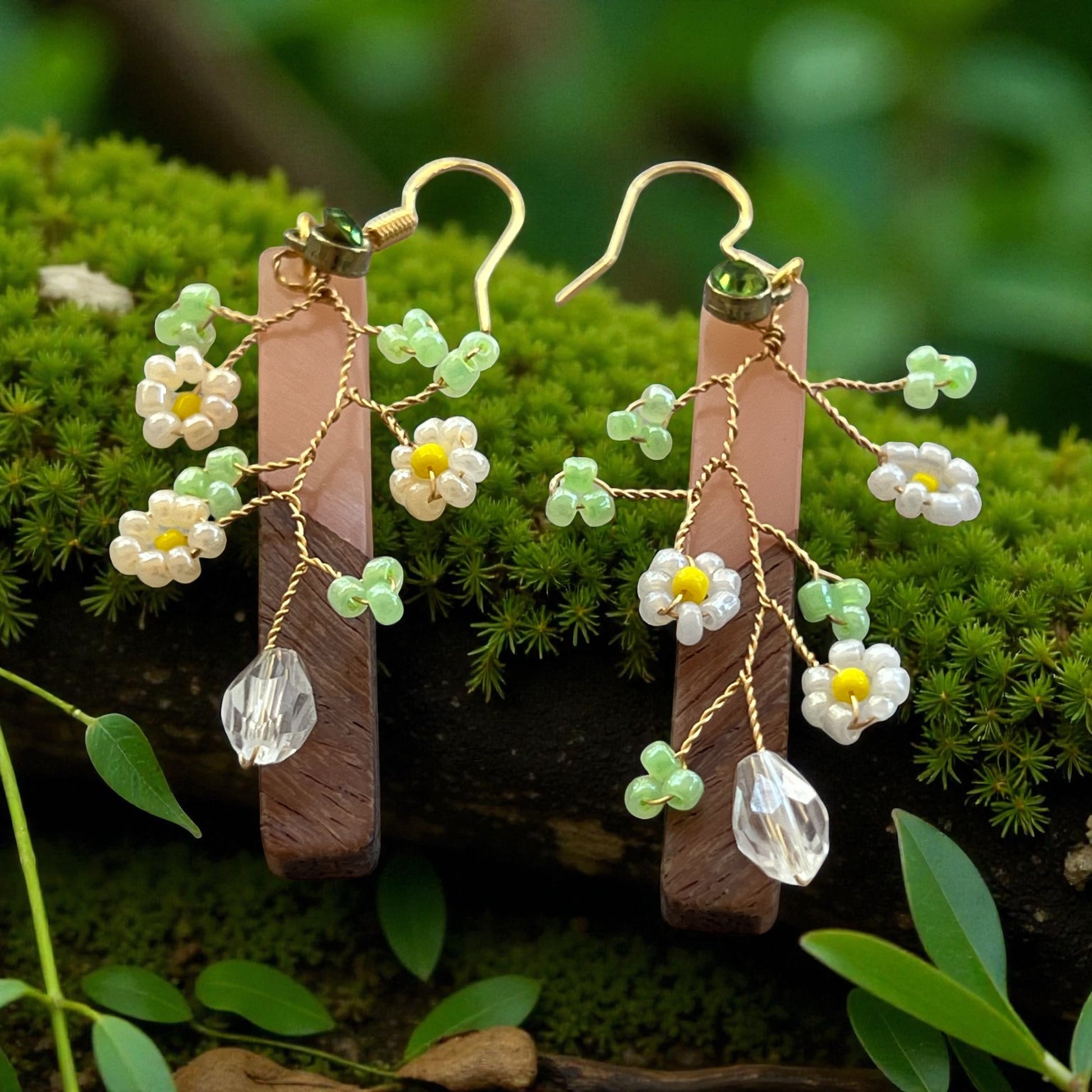 Floral earrings with green beads and clear crystals on a wooden bar against a natural background.