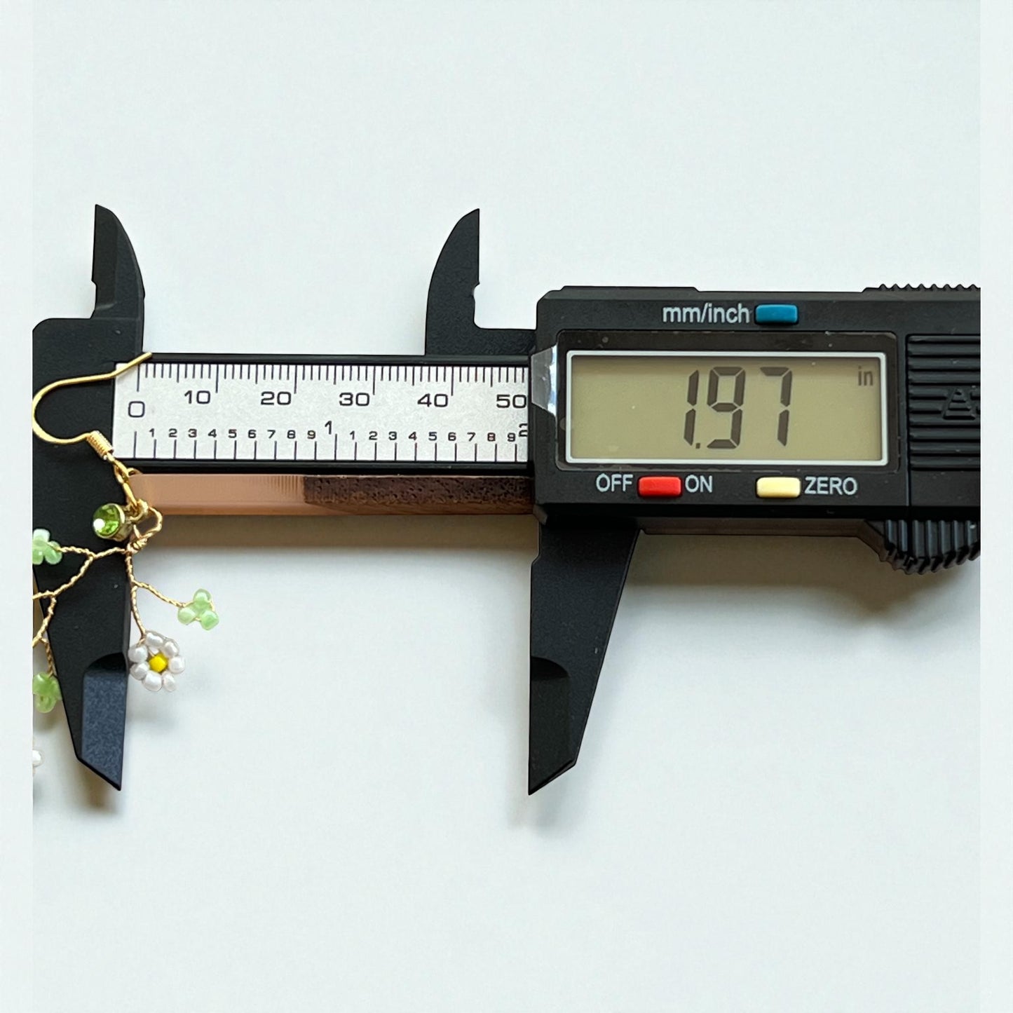 Digital caliper measuring a piece of jewelry on a white background