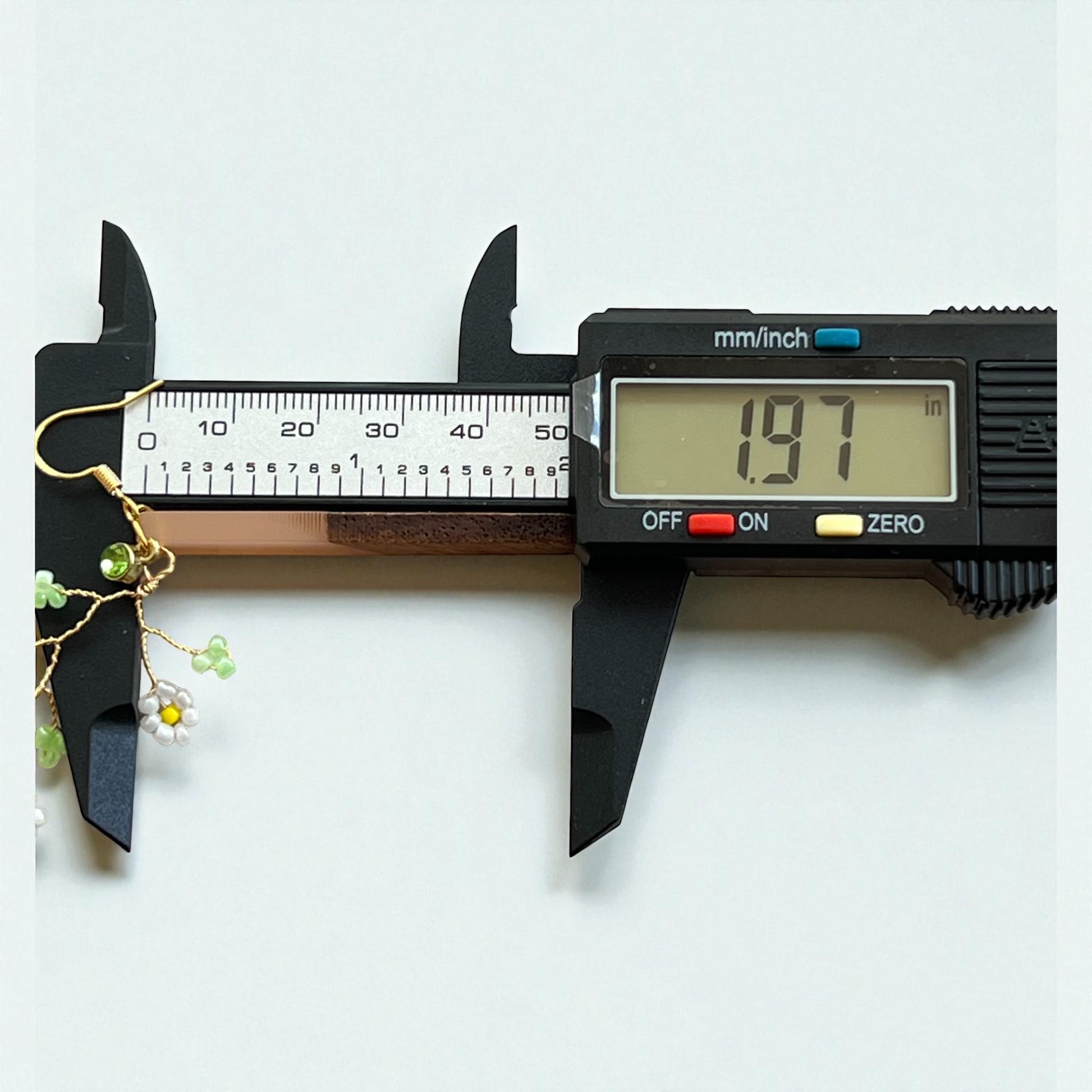 Digital caliper measuring a piece of jewelry on a white background