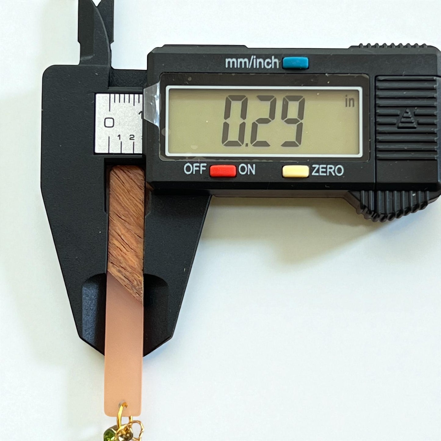 Digital caliper measuring a wooden stick with a white background