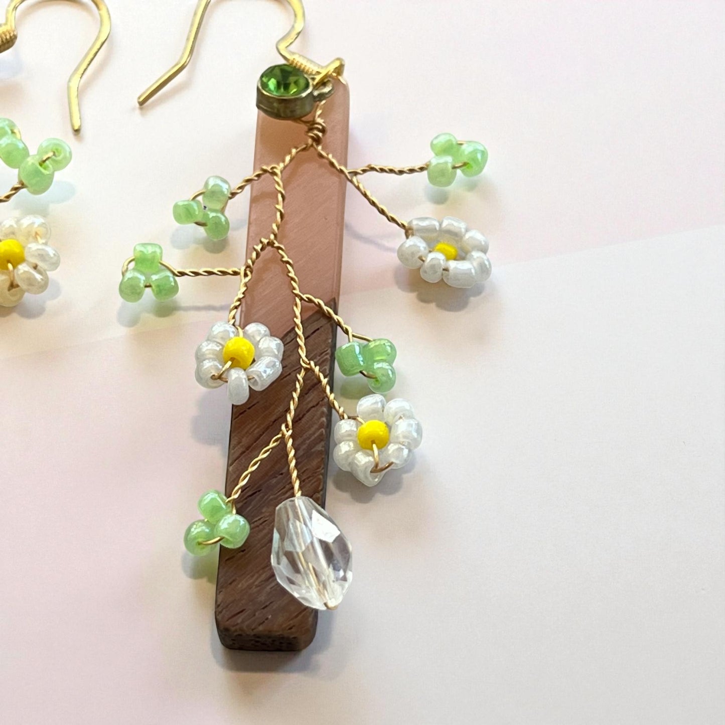 Handmade earrings with floral designs and green beads on a wooden stand against a light background