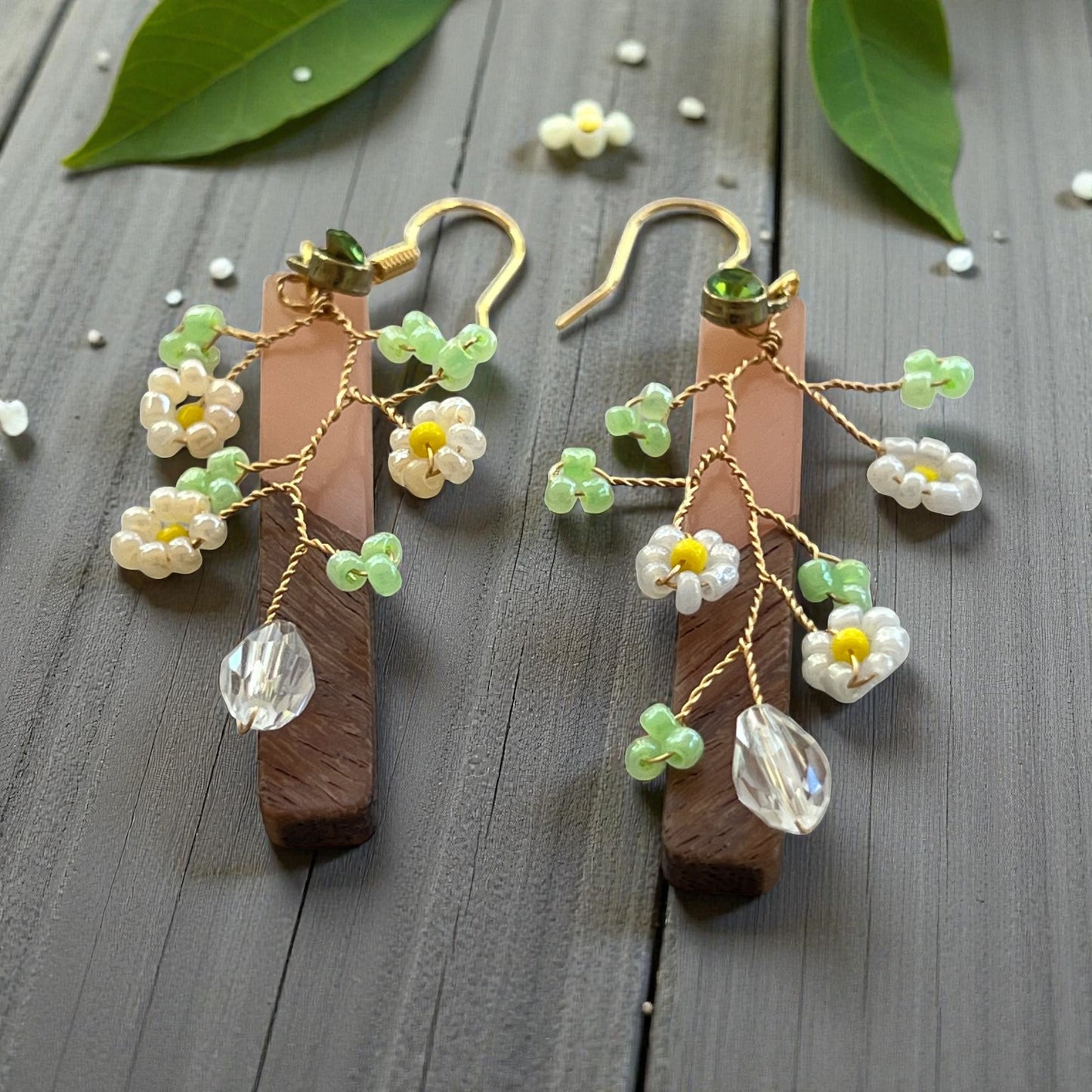 Wooden earrings with floral and crystal details on a wooden surface.