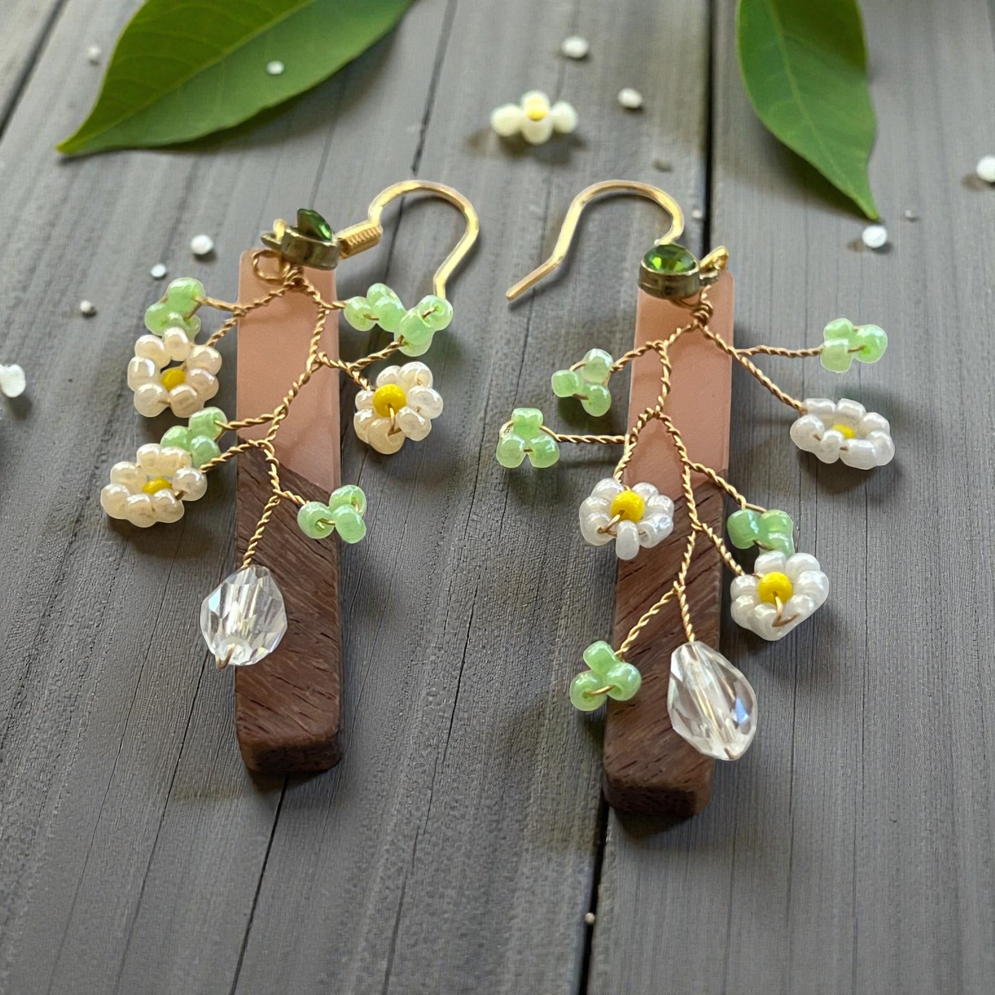 Wooden earrings with floral and crystal details on a wooden surface.
