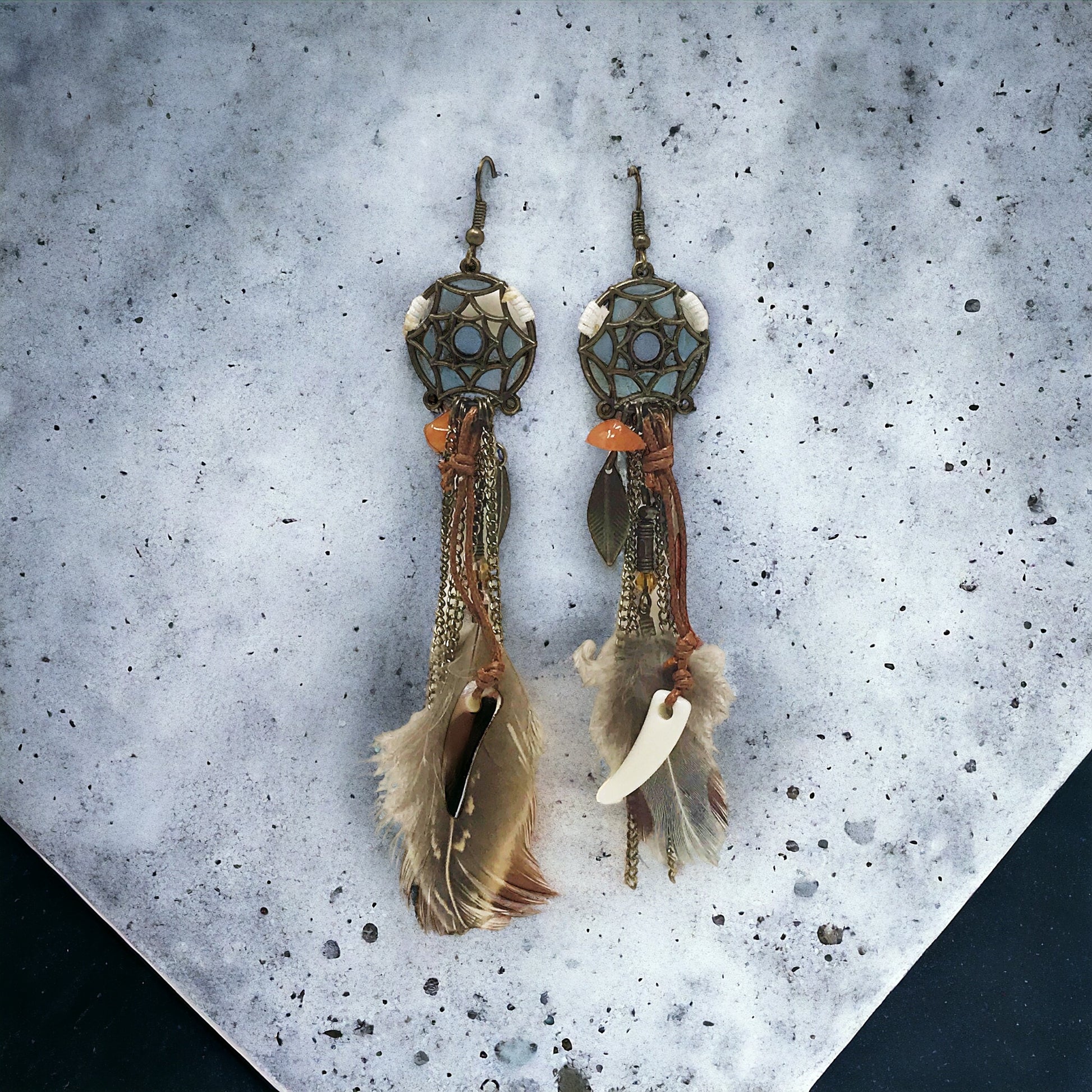 Rustic western feather earrings hanging on a wood-textured background, highlighting the drop length and design