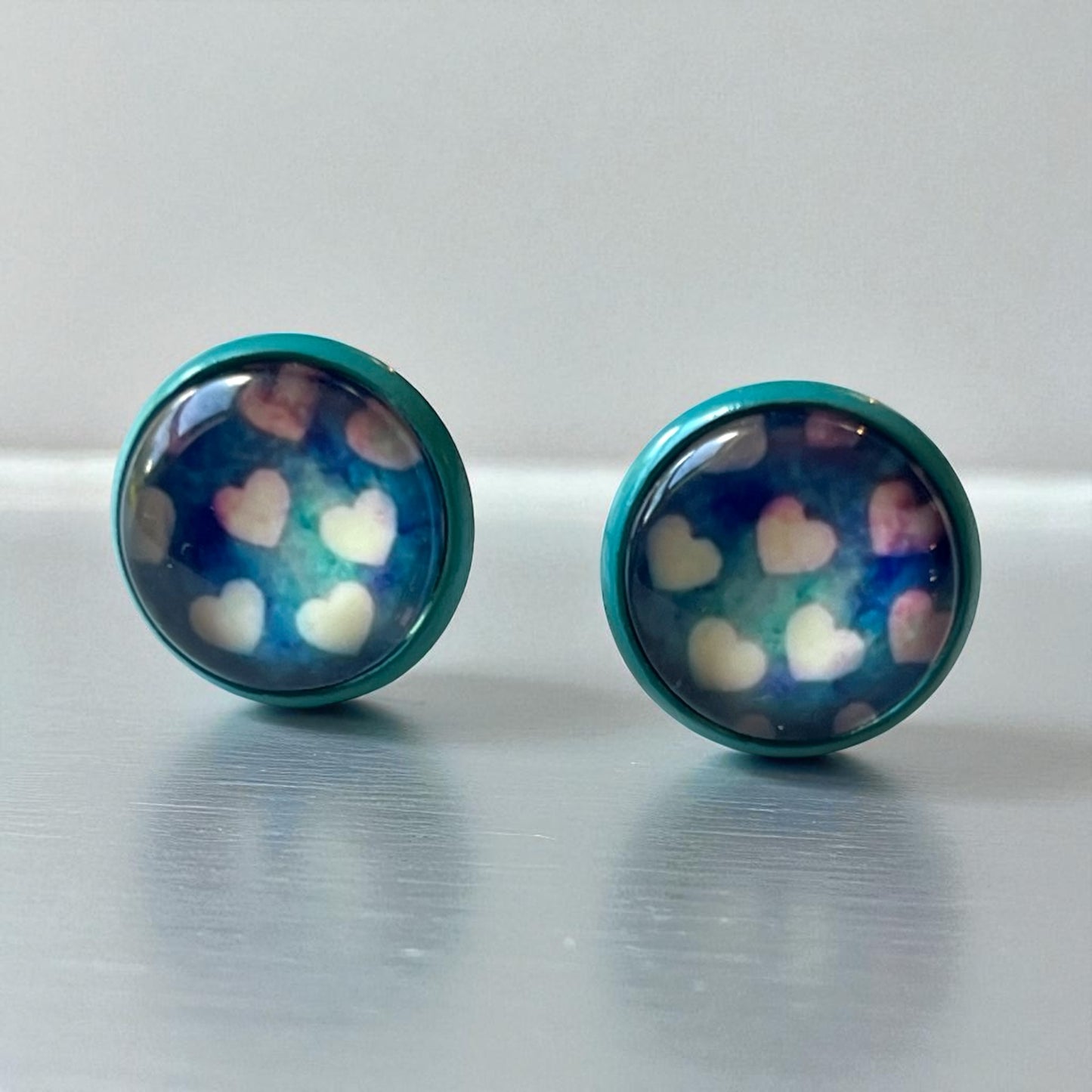 Pair of round earrings with heart pattern on a reflective surface