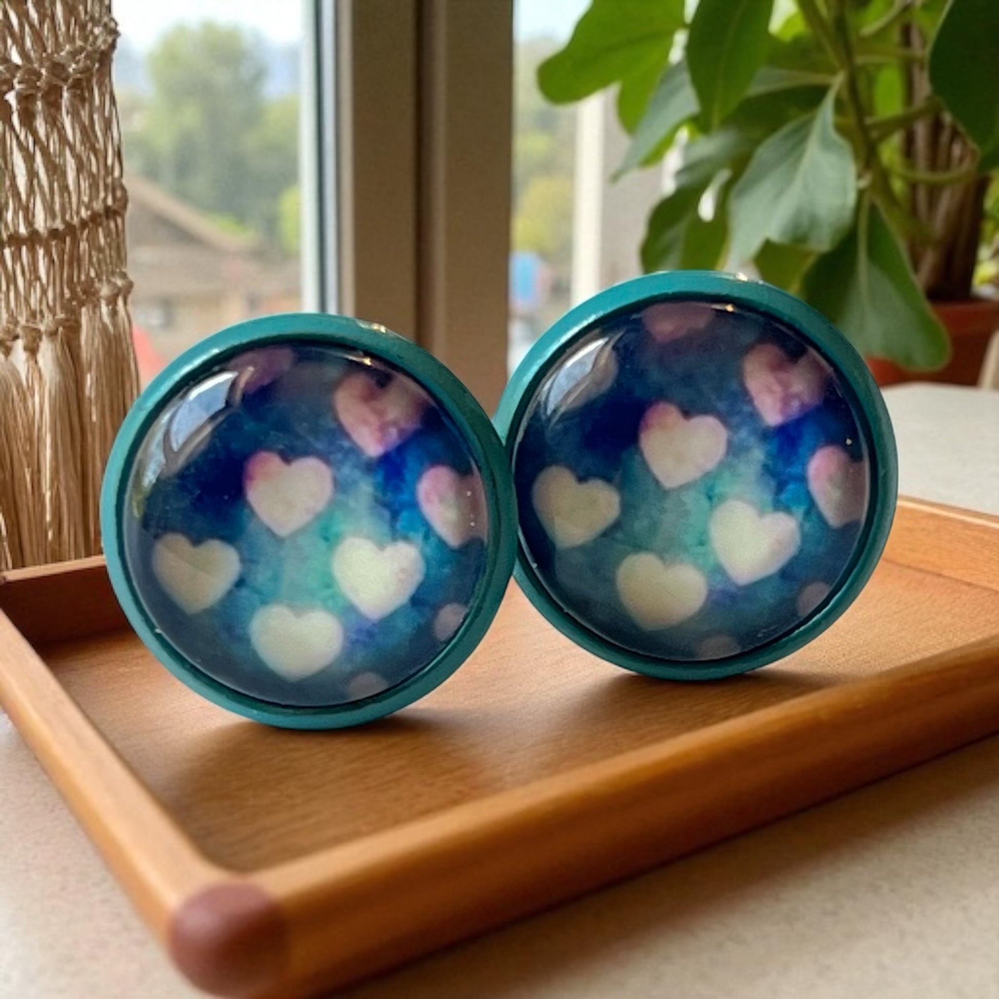 Pair of teal earrings with heart patterns on a wooden tray.