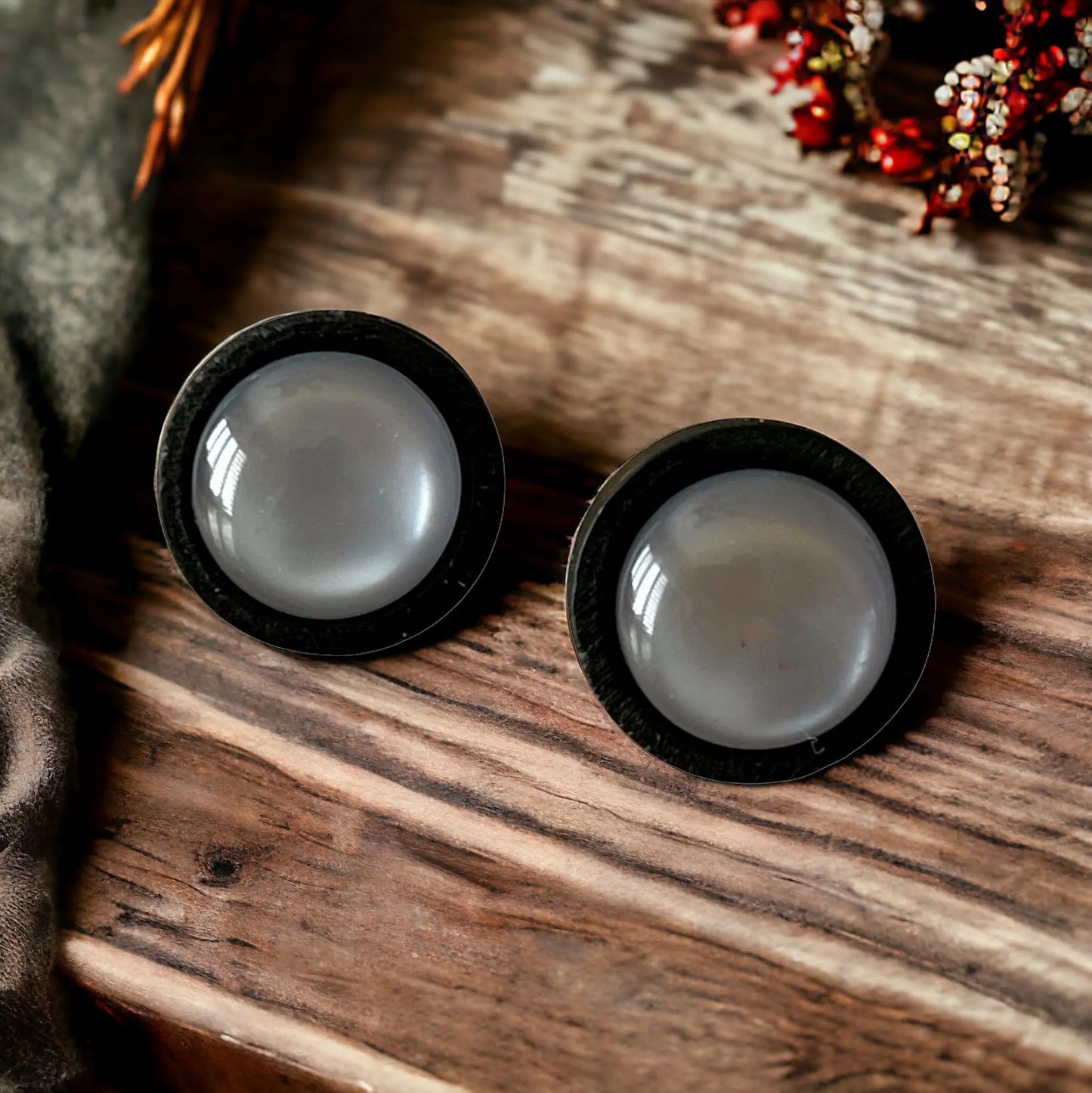 Two black-rimmed gray earrings on a wooden surface with decorative elements.