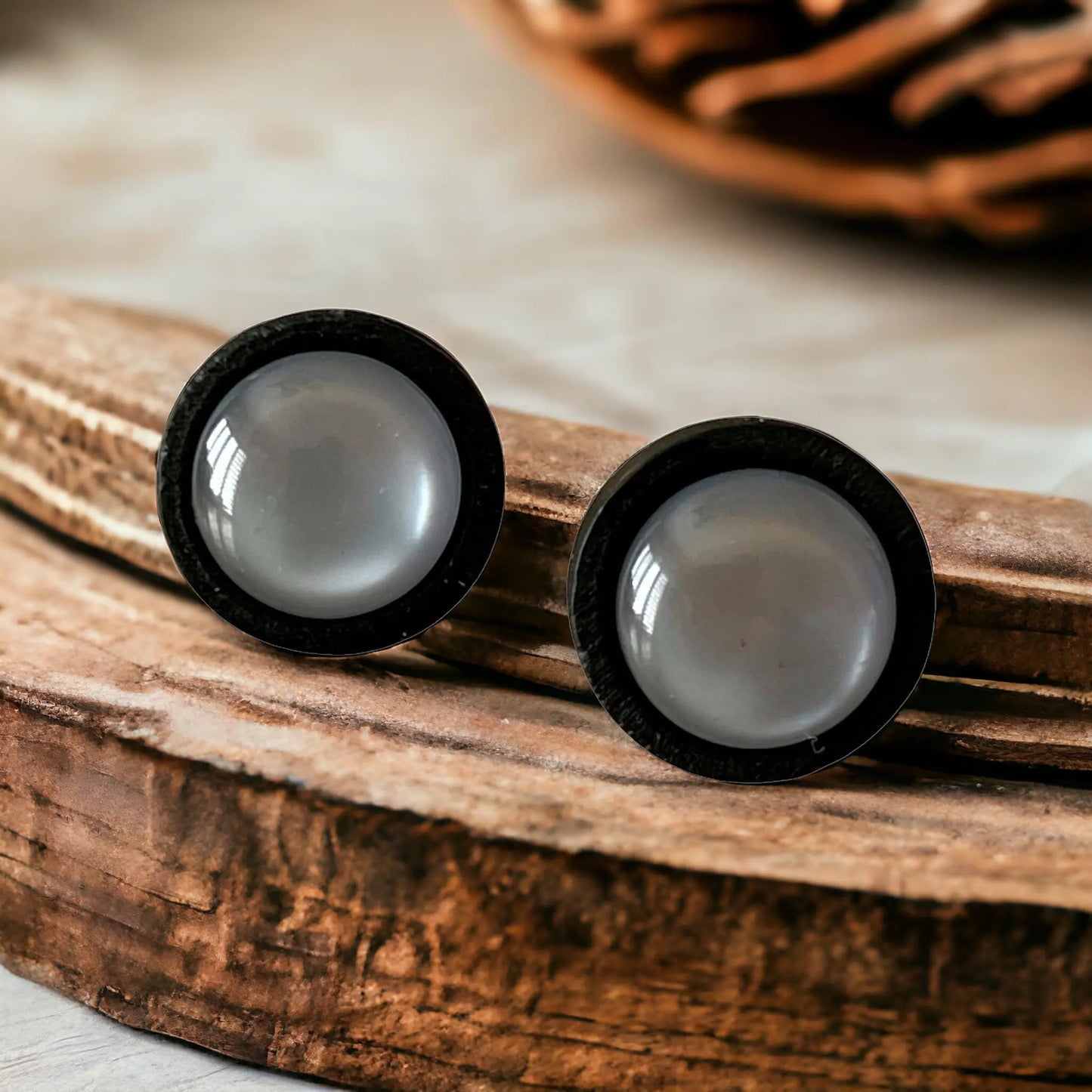 Round gray resin stud earrings with black wood border displayed on rustic wood