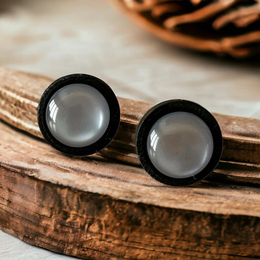 Round gray resin stud earrings with black wood border displayed on rustic wood