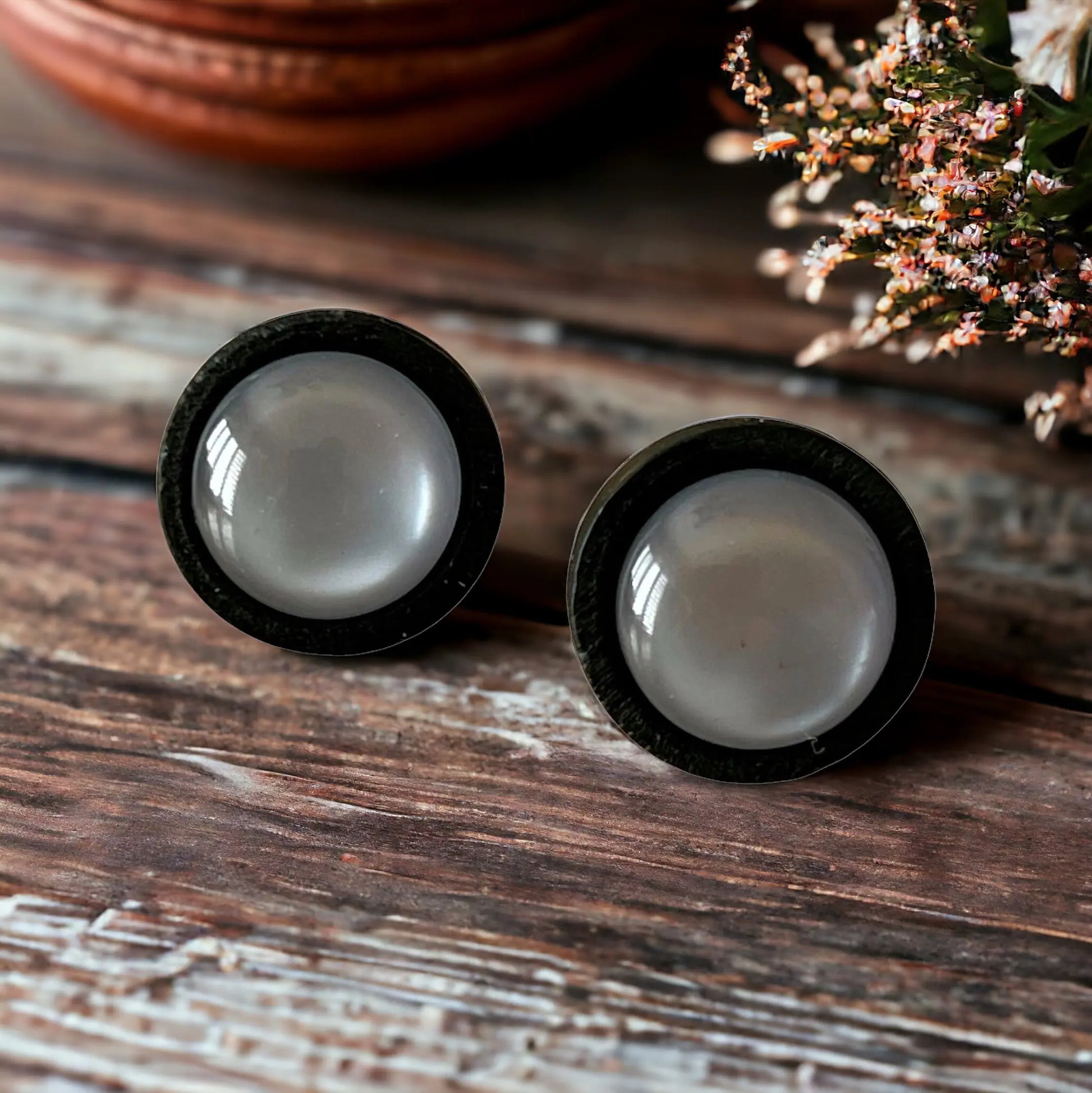 Two black-rimmed gray earrings on a wooden surface with blurred background