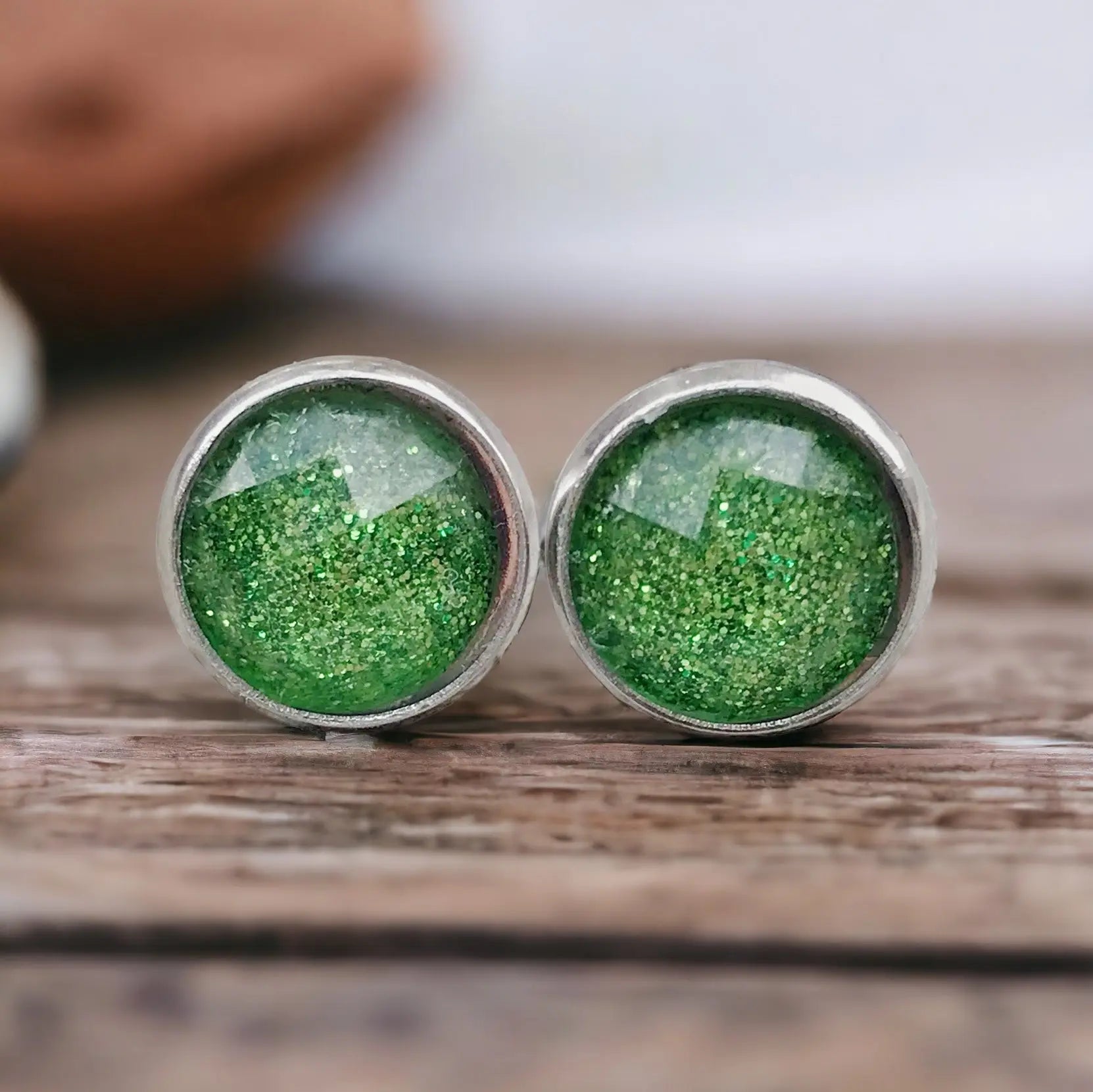 Green glittery stud earrings on a wooden surface