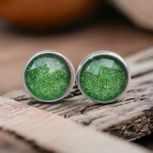 Round green glitter stud earrings in a silver-tone setting displayed on rustic wood