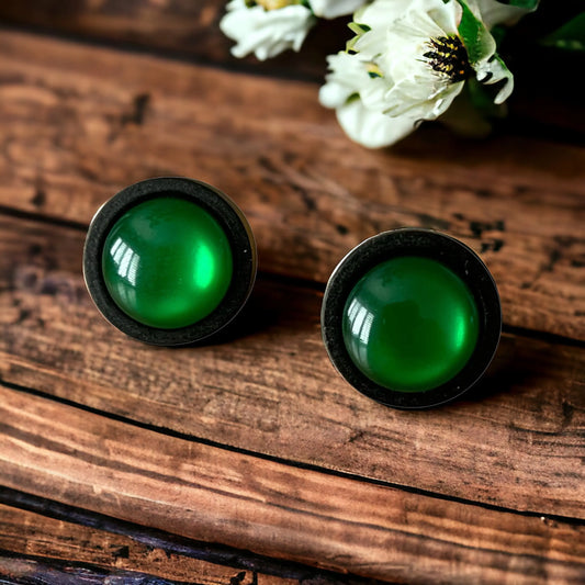 Round green resin stud earrings with black wood border displayed on rustic wood
