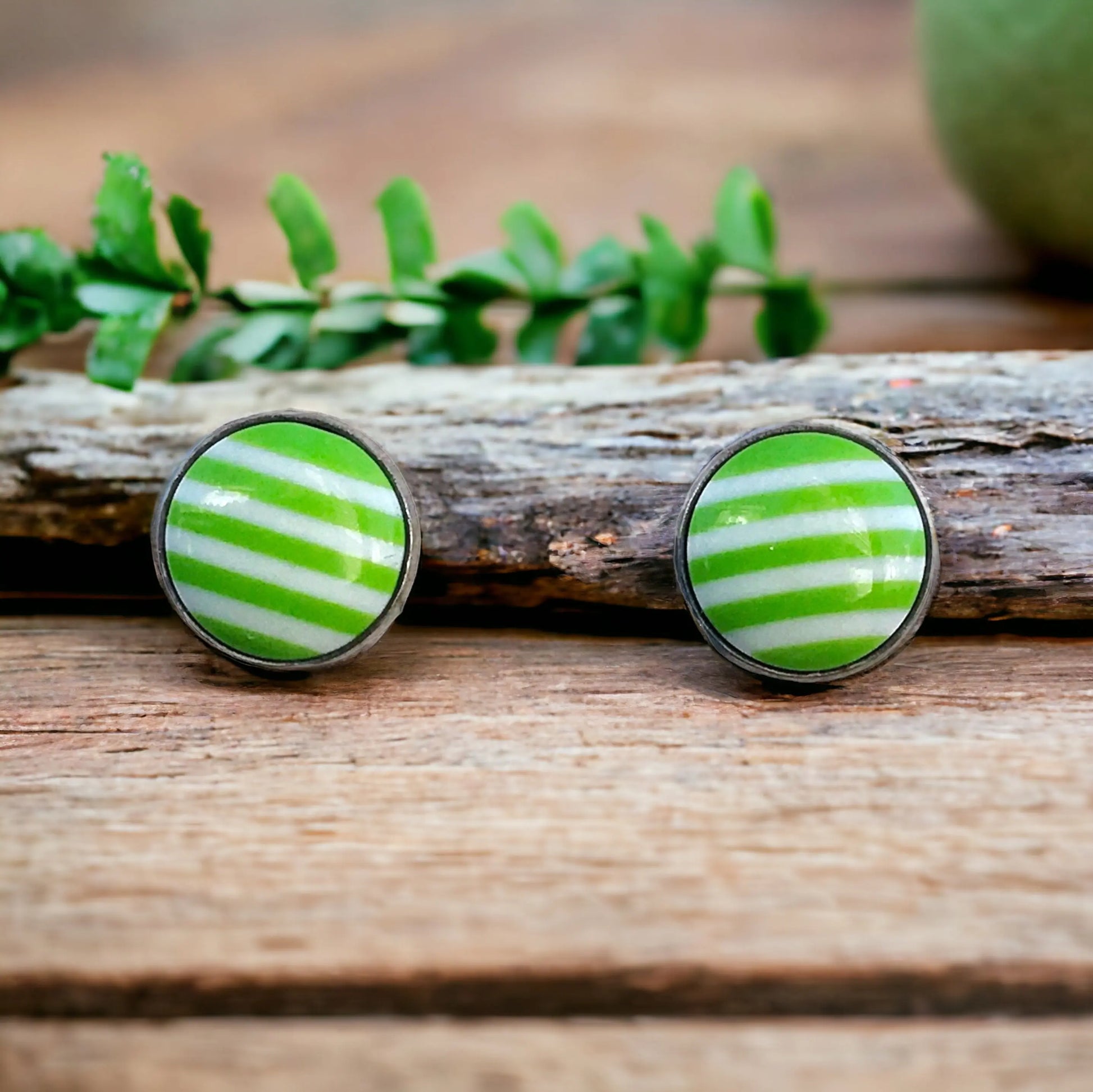 Green and white striped earrings on a wooden surface with leaves in the background
