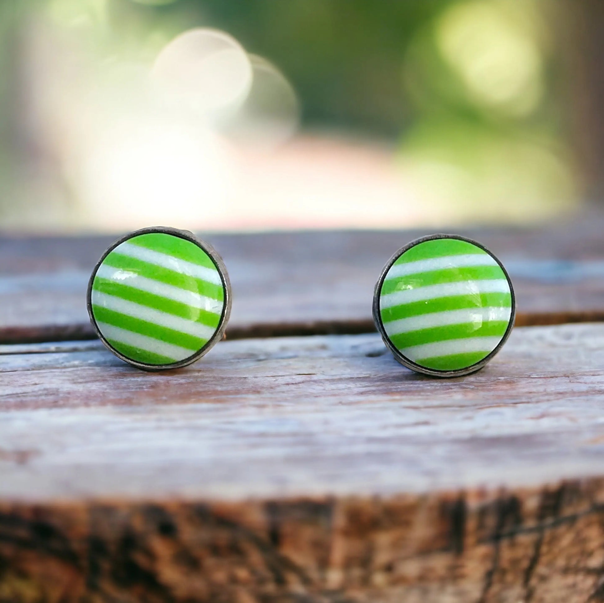 Green and white striped earrings on a wooden surface with a blurred natural background