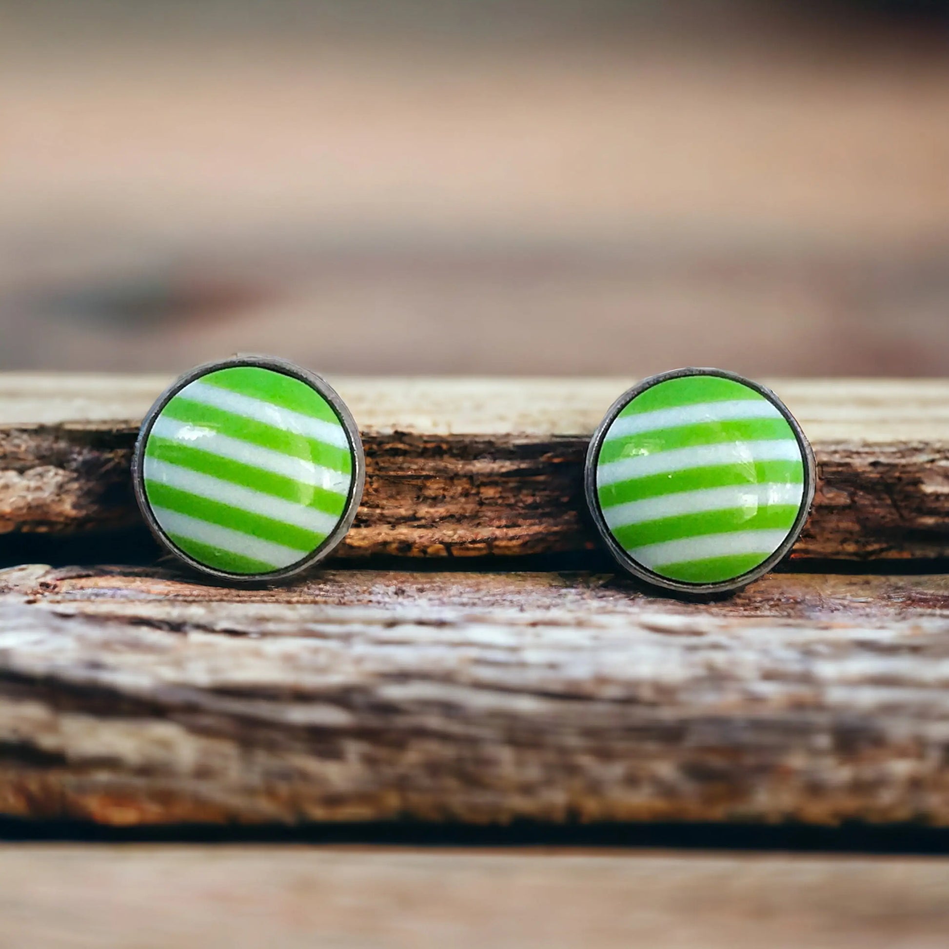 Round green and white striped stud earrings in a silver-tone setting displayed on a rustic wood surface