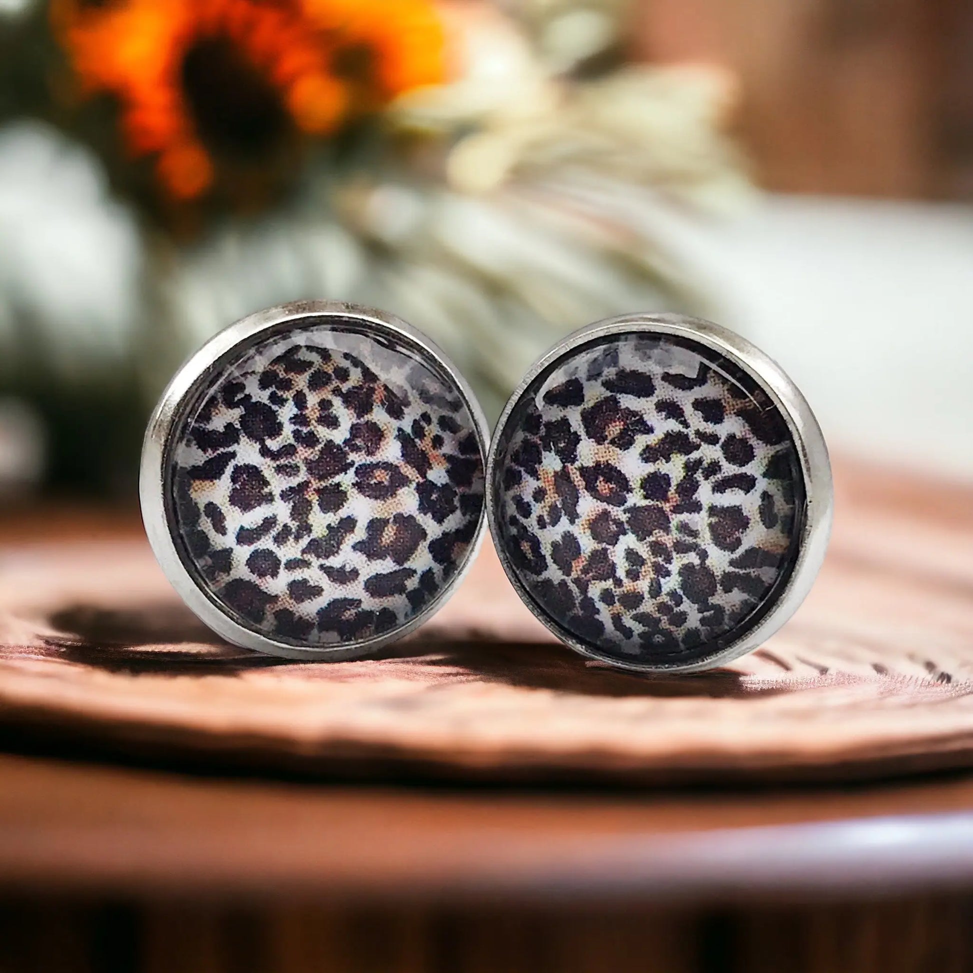 Pair of earrings with leopard print design on a wooden surface.