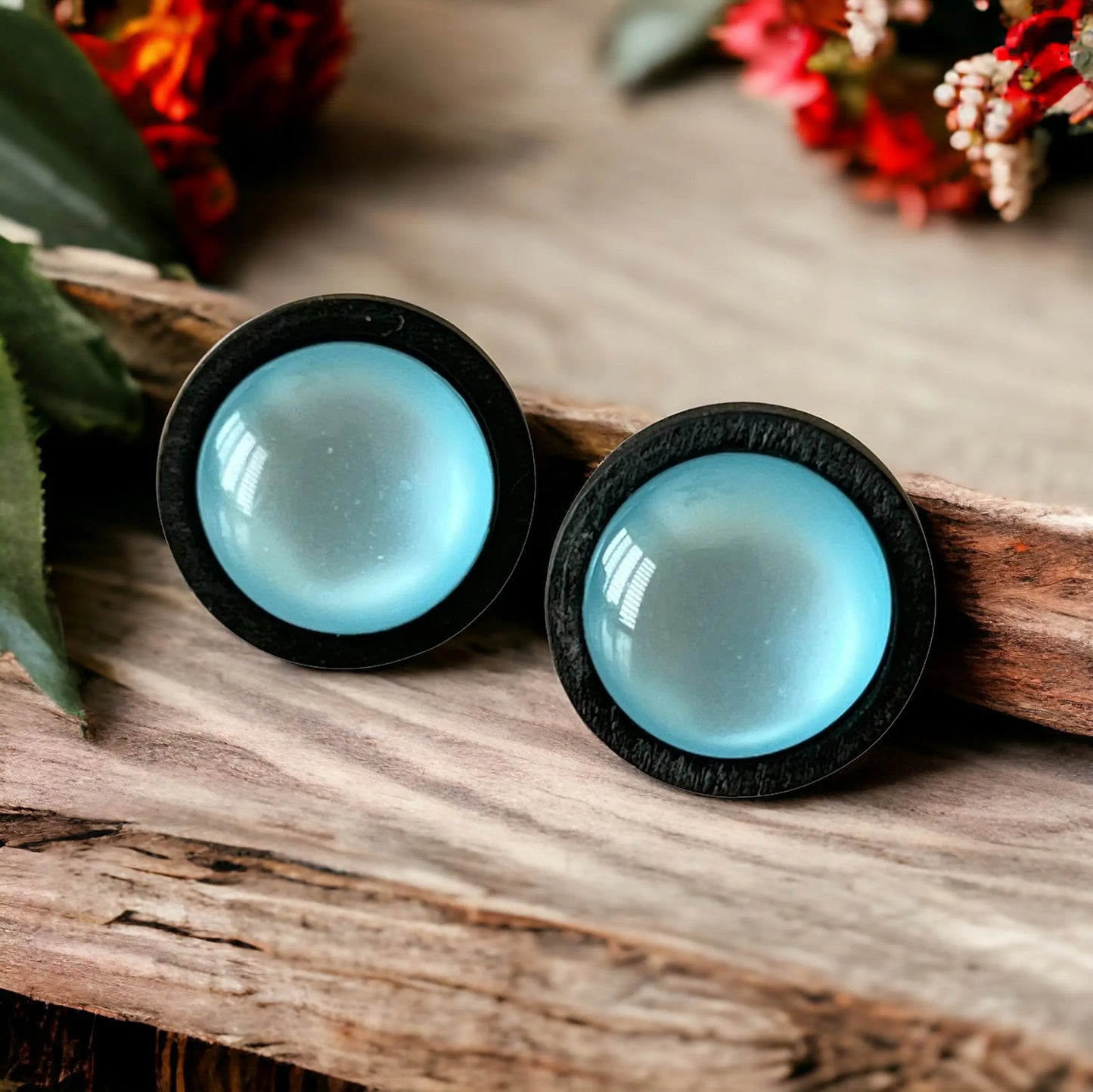 Pair of blue earrings with black rims on a boho wooden surface.
