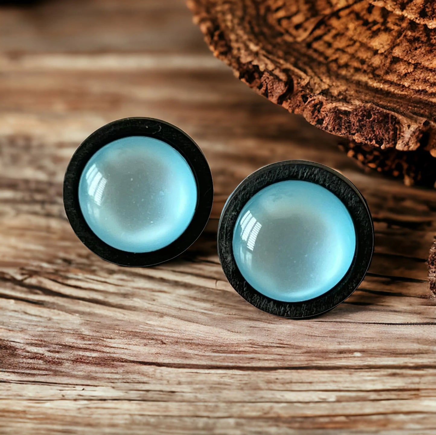 Pair of earrings with black rims and light blue centers on a wooden surface.