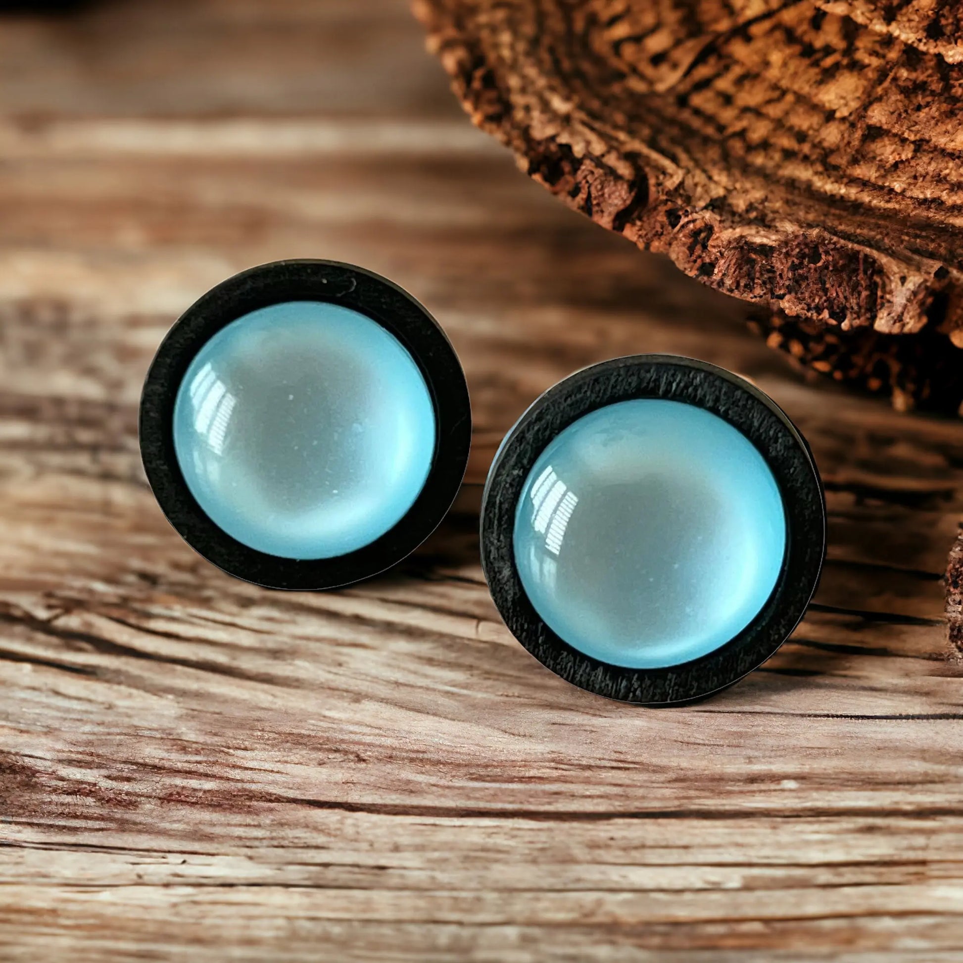 Pair of earrings with black rims and light blue centers on a wooden surface.