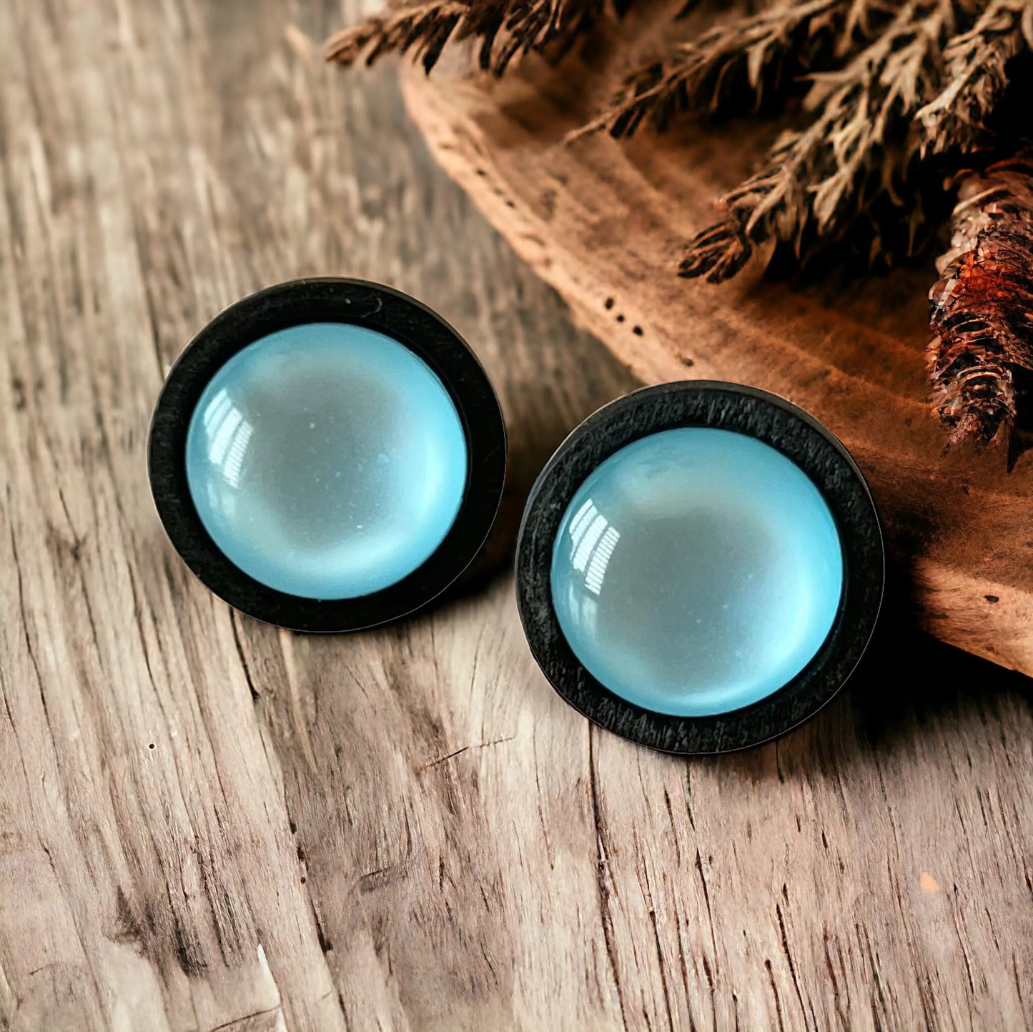 Pair of blue earrings with black rims on a rustic wooden surface