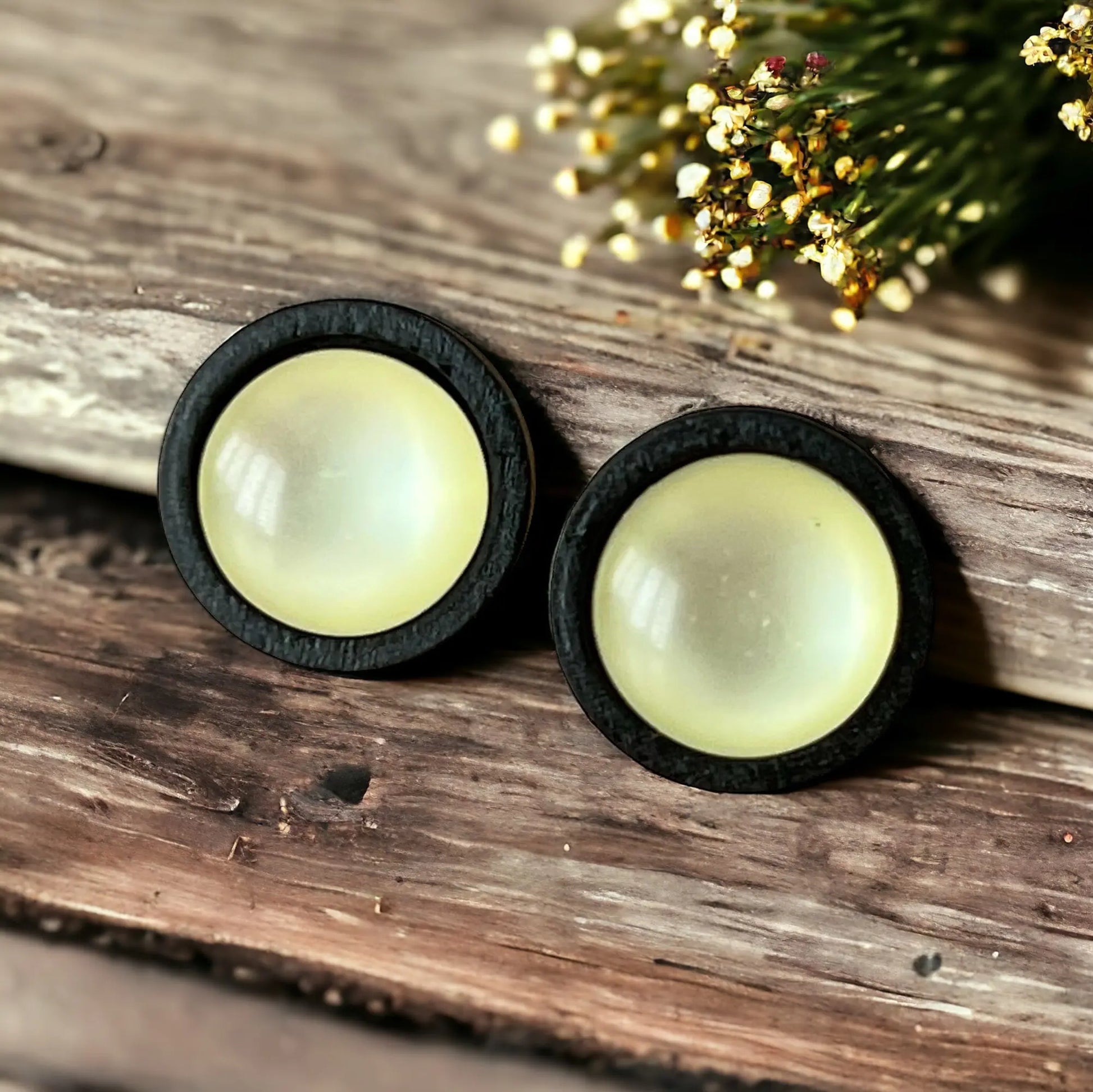 Pair of round earrings with black rims on a wooden surface with flowers in the background