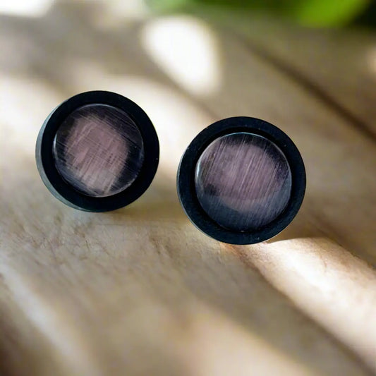 Pair of black earrings with purple gray glass on a wooden surface