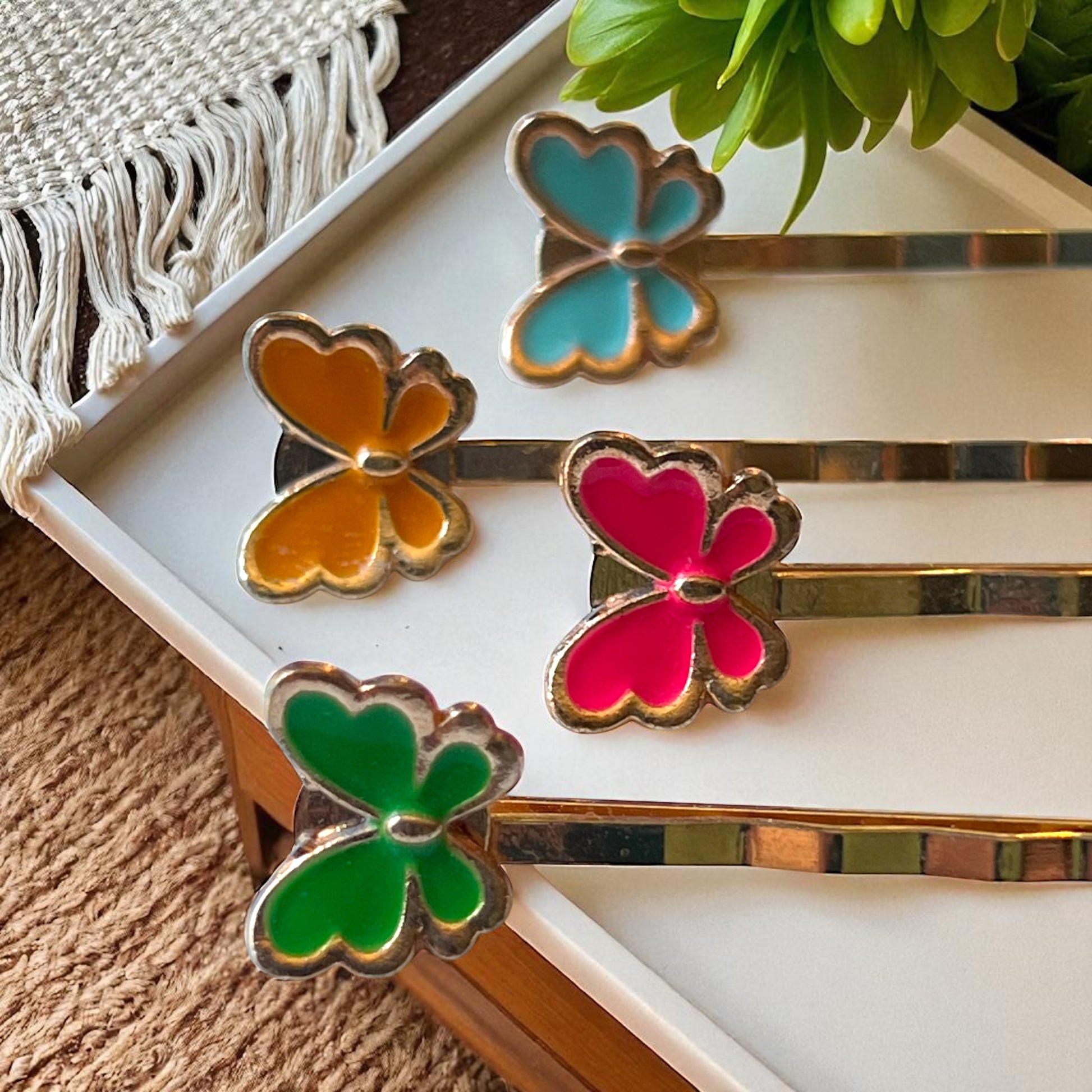 Butterfly-shaped hair pins in gold and colorful enamel on a white tray.