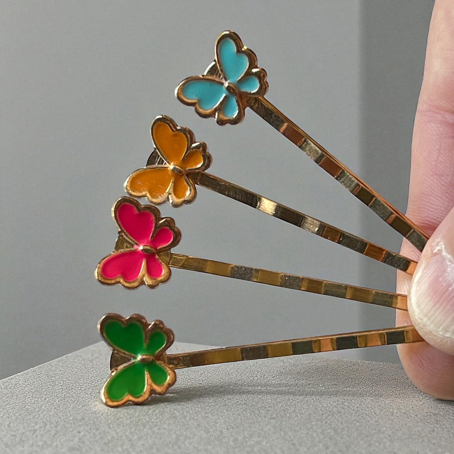 Butterfly-shaped hair pins with colorful enamel on a gray background