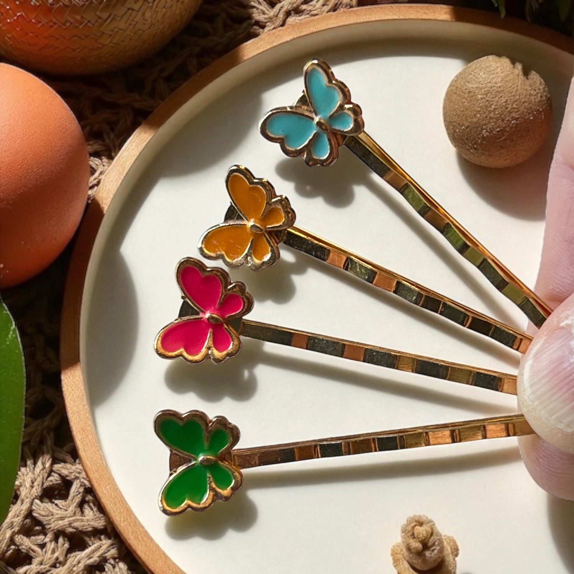 Colorful butterfly-shaped hair pins on a white plate with a hand holding one of them.