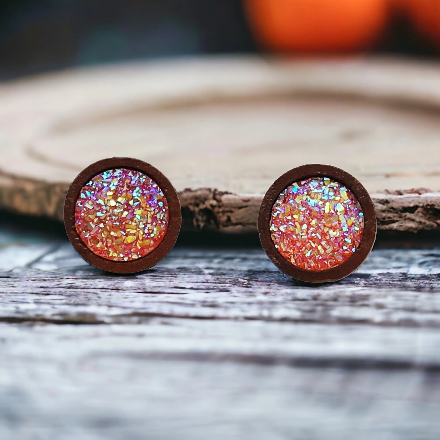 Front of round orange druzy wood stud earrings displayed on a rustic wood surface