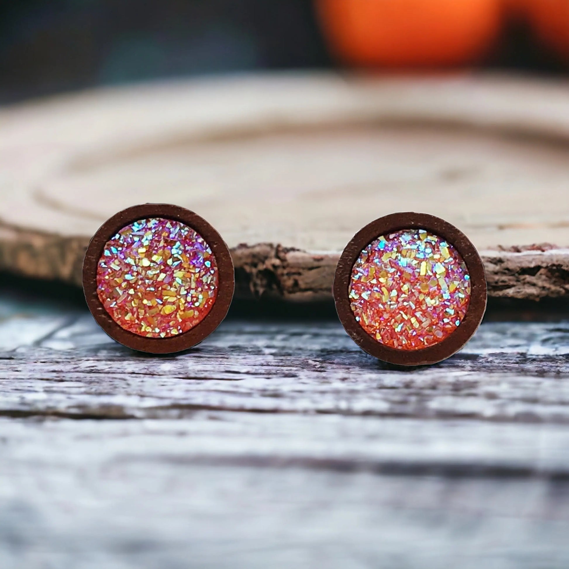 Front of round orange druzy wood stud earrings displayed on a rustic wood surface