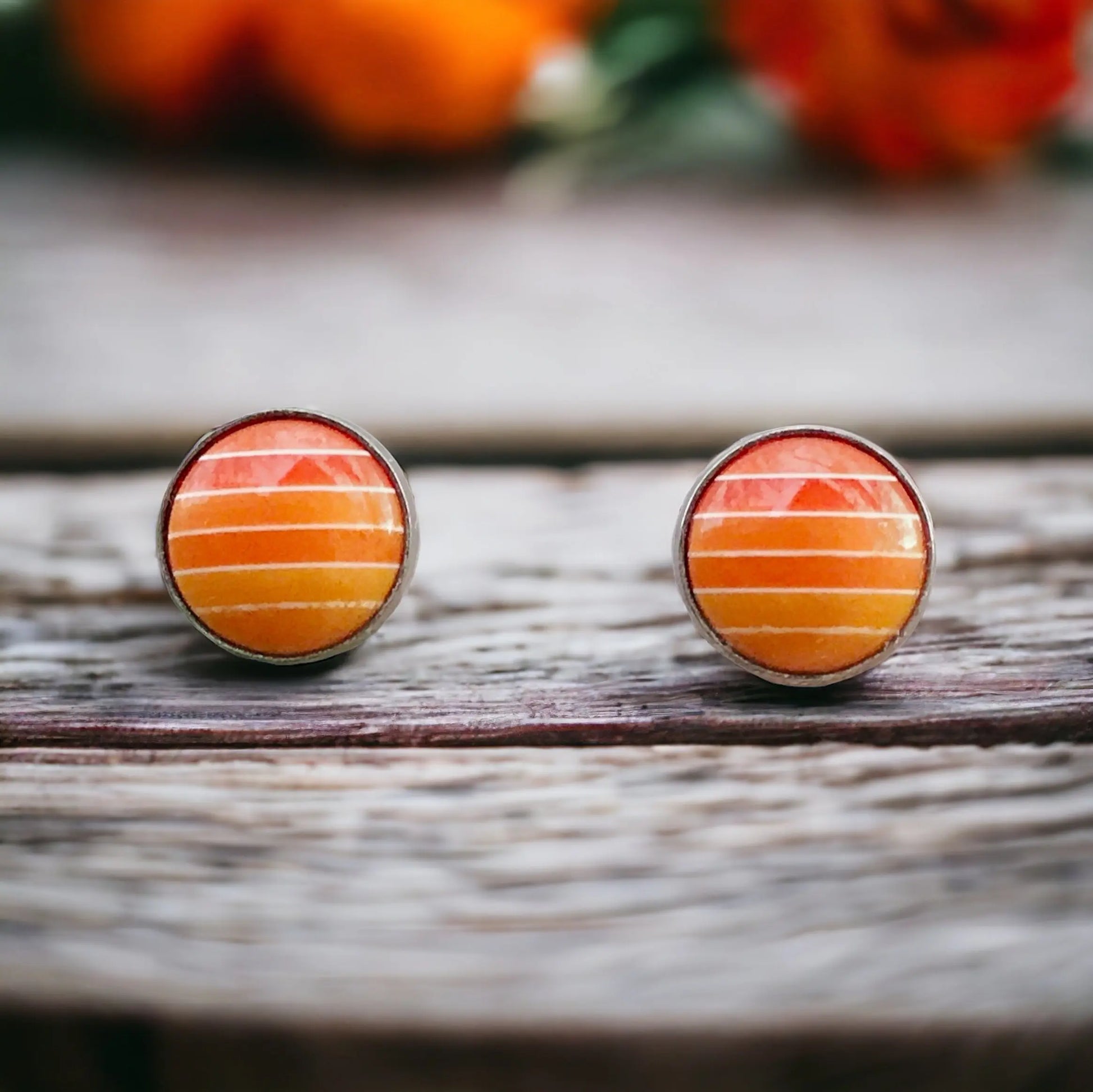 Round orange gradient striped stud earrings in a silver-tone setting displayed on a rustic wood display 