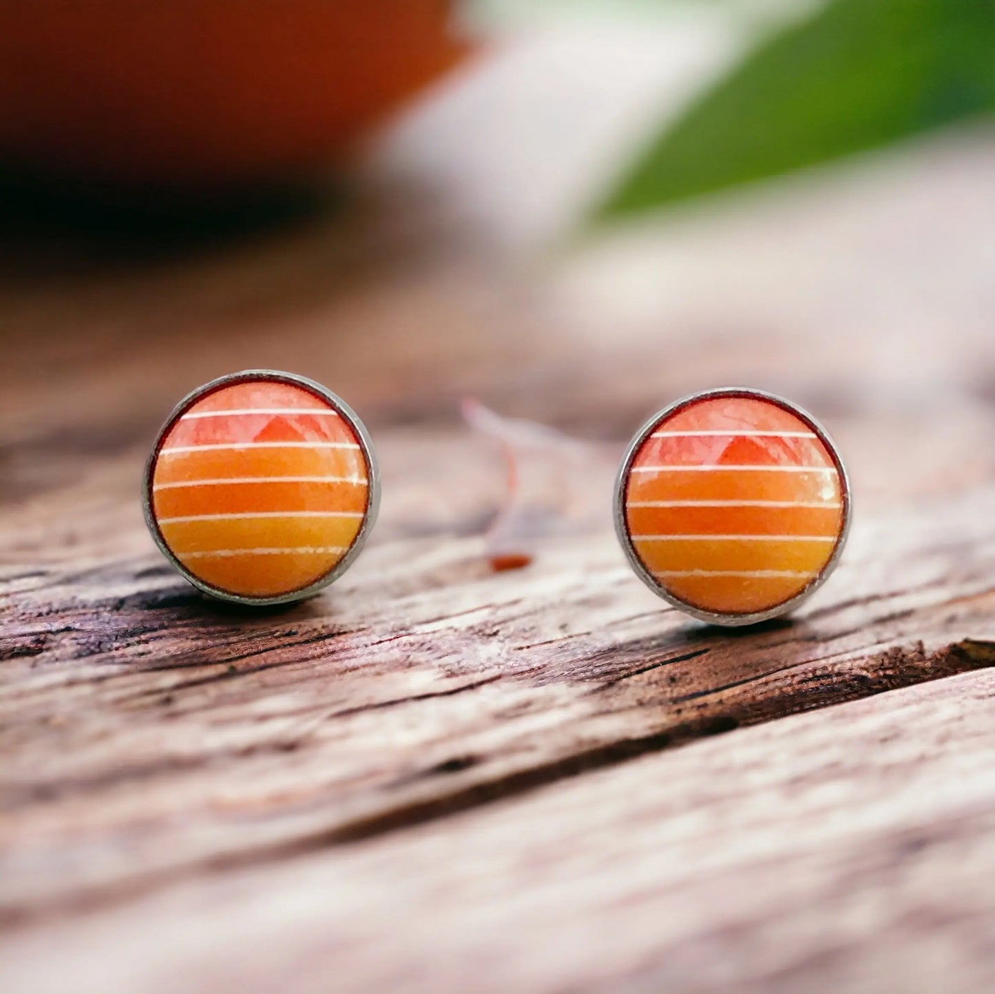 Round orange gradient striped stud earrings in a silver-tone setting displayed on a wood surface